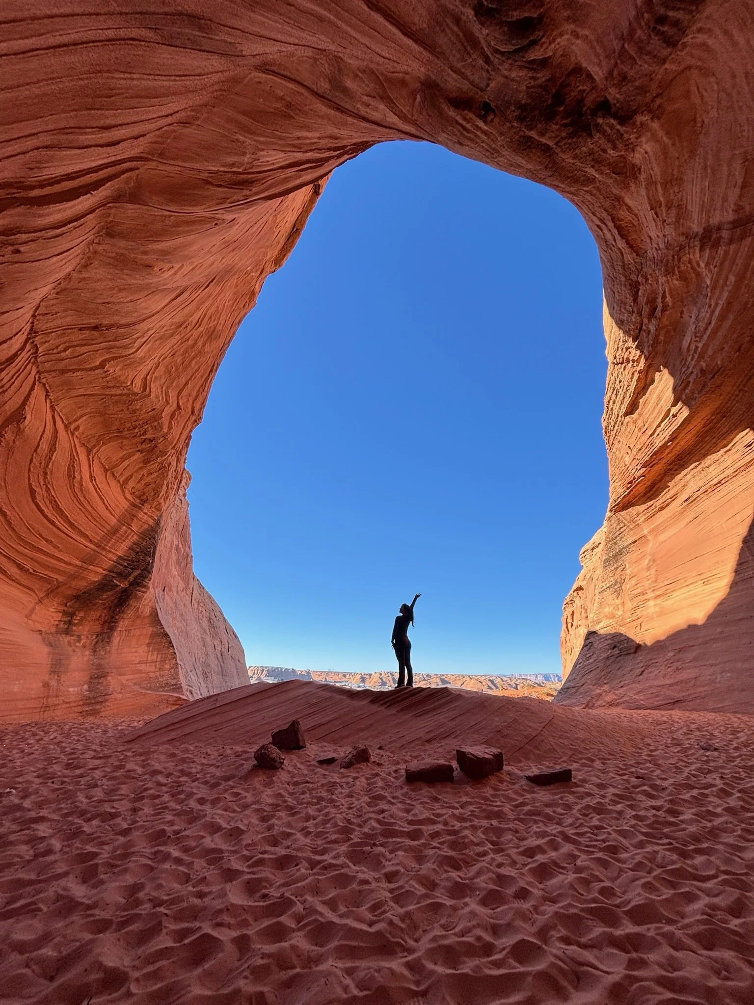 A person standing beneath a sandstone arch against a clear blue sky.