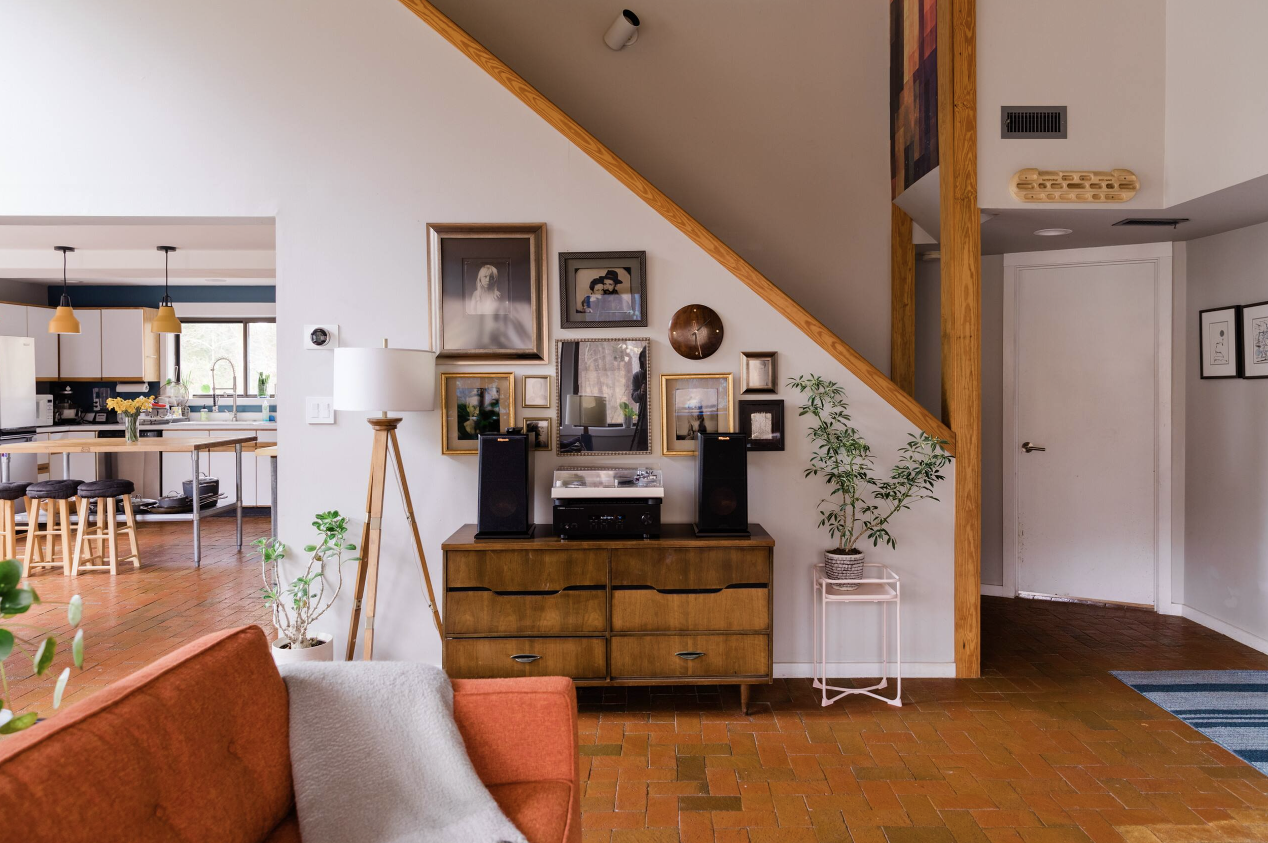 Living room with a wooden TV stand, pictures on the wall, a potted plant, and a section of a red couch with a white pillow in the foreground.