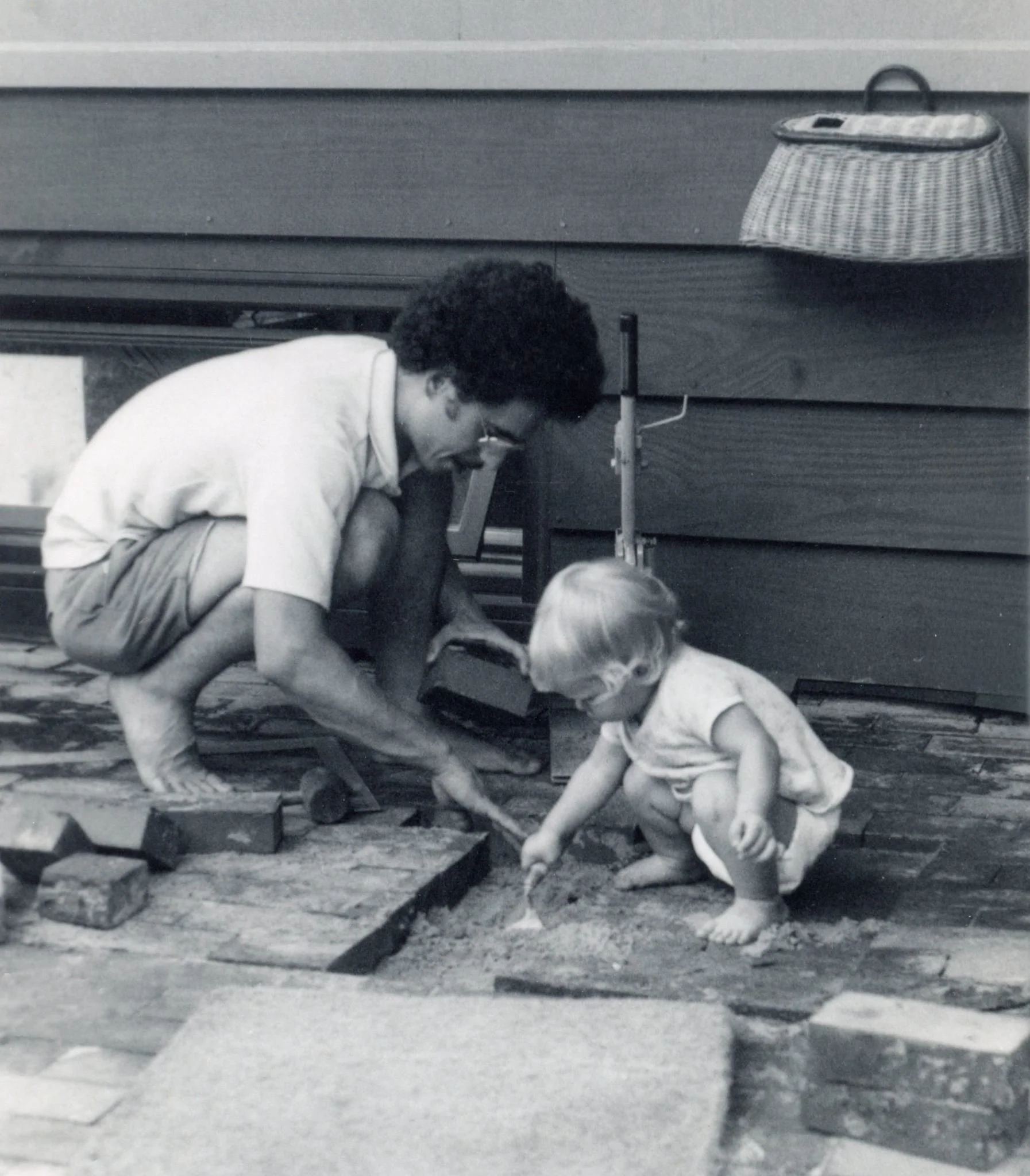 A person is kneeling on the ground with a child, digging in the ground on a building site.