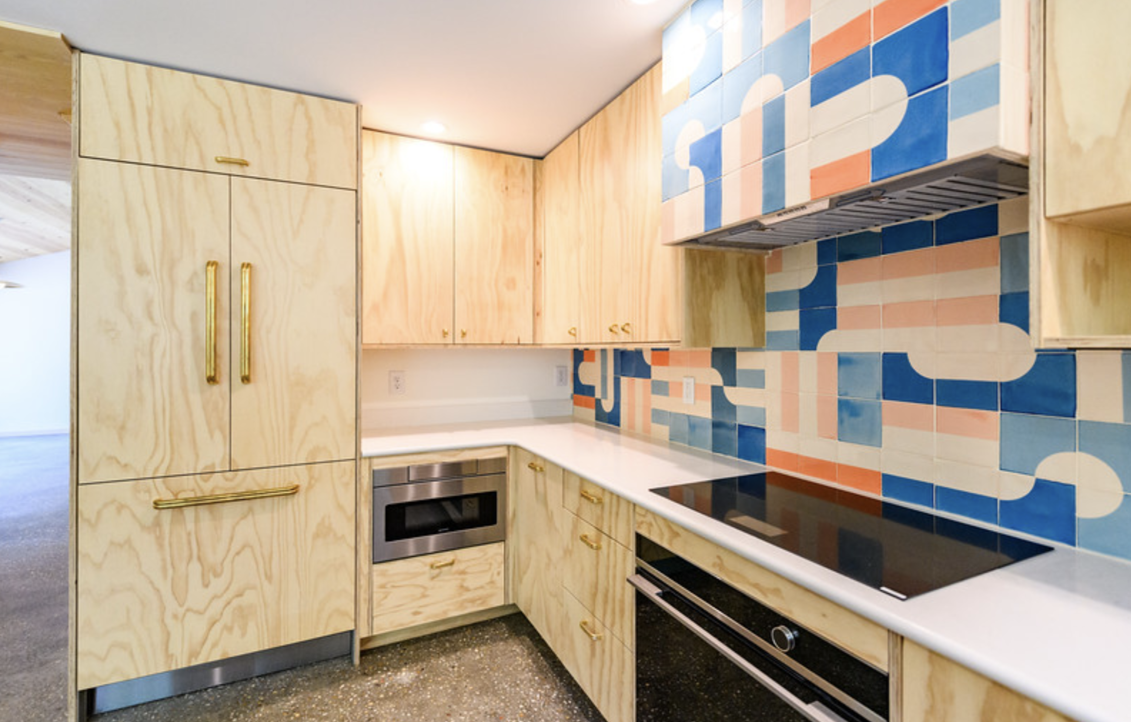 Modern kitchen with light wood cabinets, a colorful geometric tile backsplash, and stainless steel appliances.