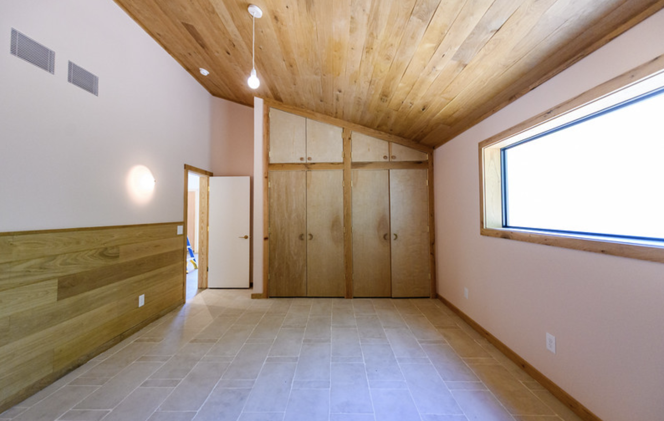 A room with a wooden ceiling, a large window, a built-in closet, and tile flooring.