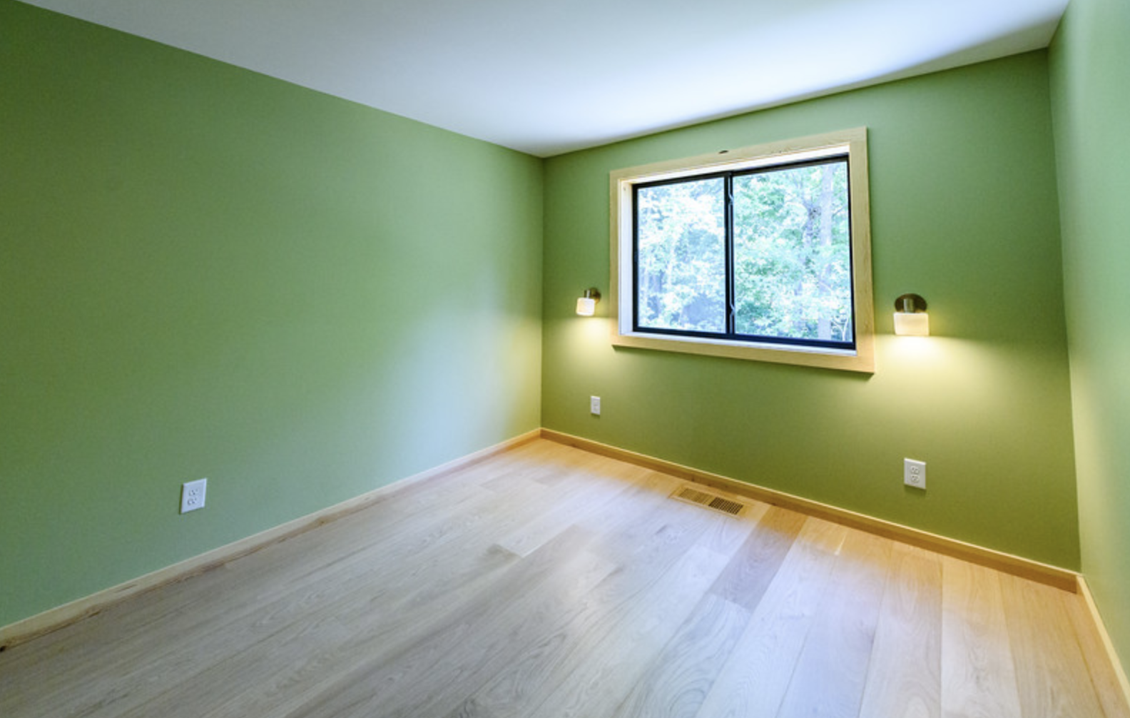 Empty room with green walls, wooden floor, window, and wall-mounted lights.