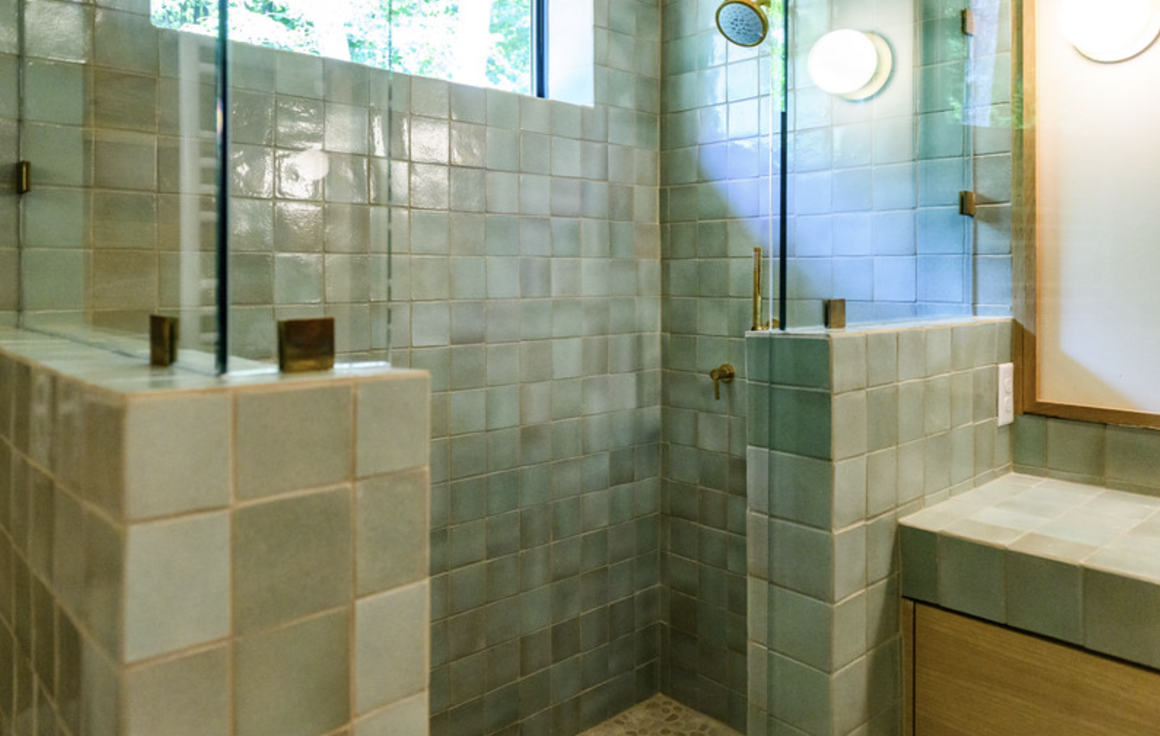 Tile shower with a glass door, overhead showerhead, and a window showing greenery outside.