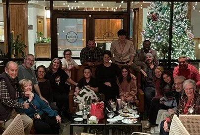 Group of people gathered around a table in a restaurant decorated for Christmas, with a Christmas tree in the background.