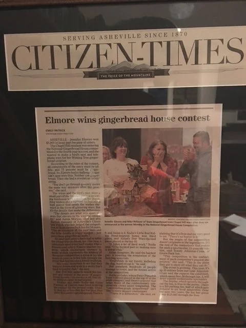Framed newspaper front page from Citizen-Times featuring a headline about Elmore winning a gingerbread house contest, with a photo of people celebrating.