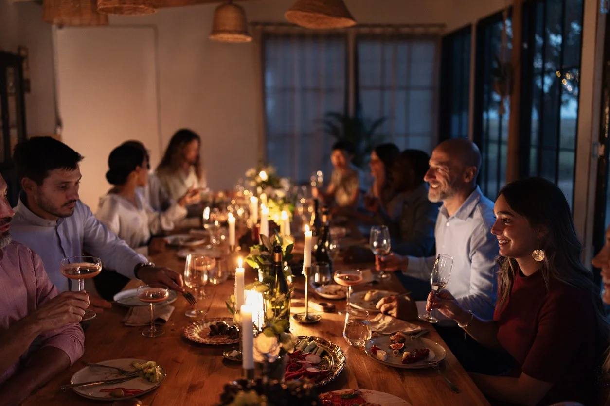 People gathered around a dinner table enjoying a candlelit meal in a cozy, warmly lit room during the evening.