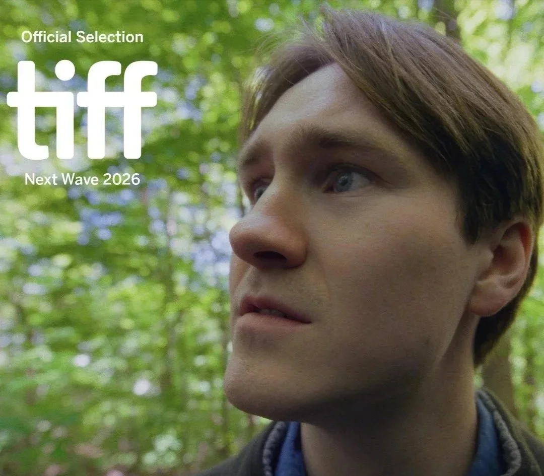 A young man with light brown hair and blue eyes looking to the side, in a green forest setting, with the text "Official Selection TIFF Next Wave 2026" in the top left corner.