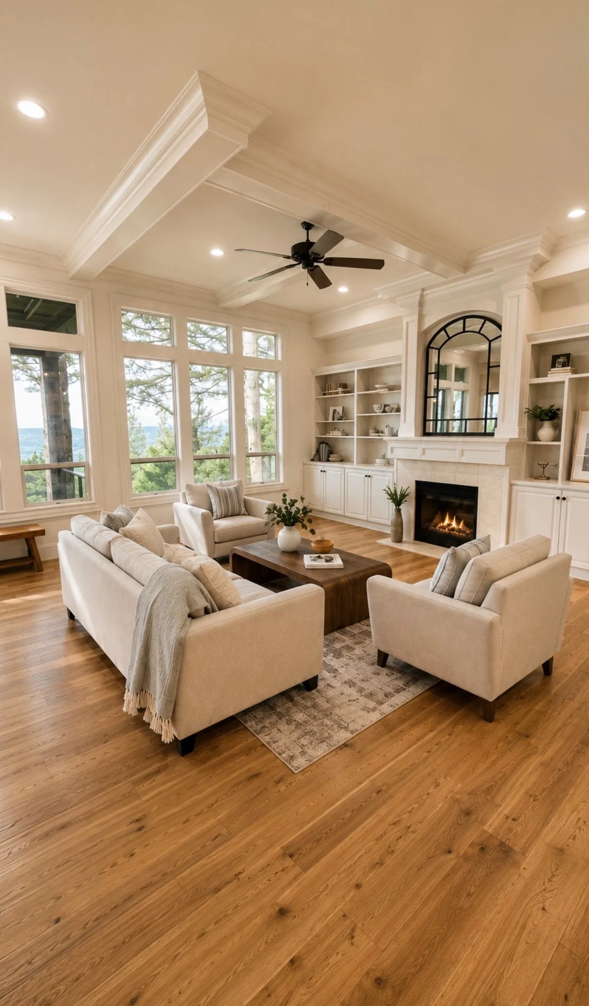 Bright living room stage with neutral seating, a wood, coffee table, fireplace, warm, wood floors, and large windows overlooking the trees.