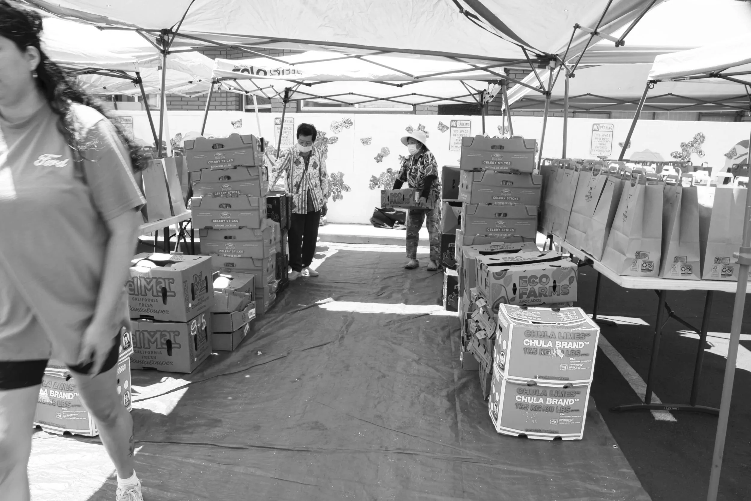 People shopping for produce at an outdoor market with boxes of celery sticks and other vegetables under tents.