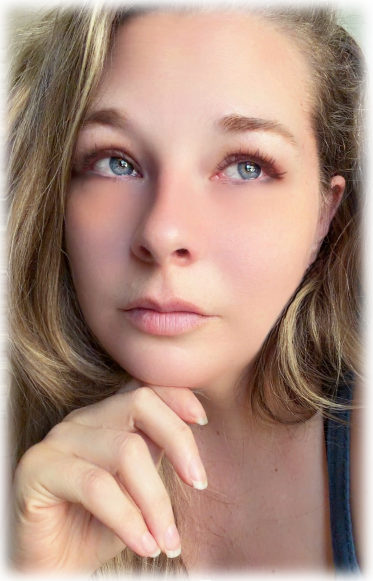 Close-up of a young woman with blonde hair, blue eyes, and light makeup, resting her chin on her hand.