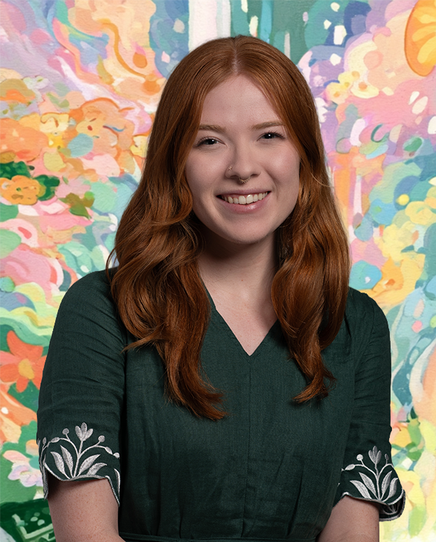 A young woman with long red hair, wearing a dark green dress with embroidered sleeves, smiling in front of a colorful, abstract painted background.