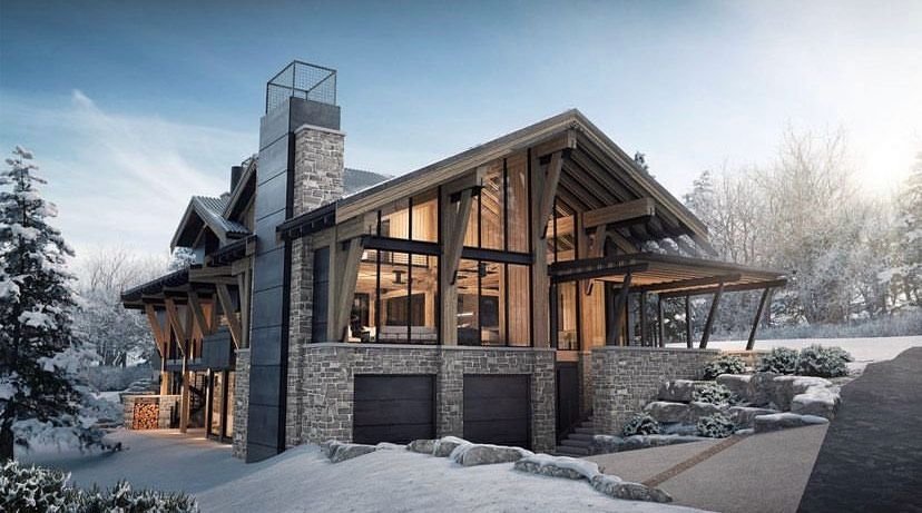 Modern mountain house with stone and wood exterior, large windows, and garage doors in a snowy landscape during sunset.