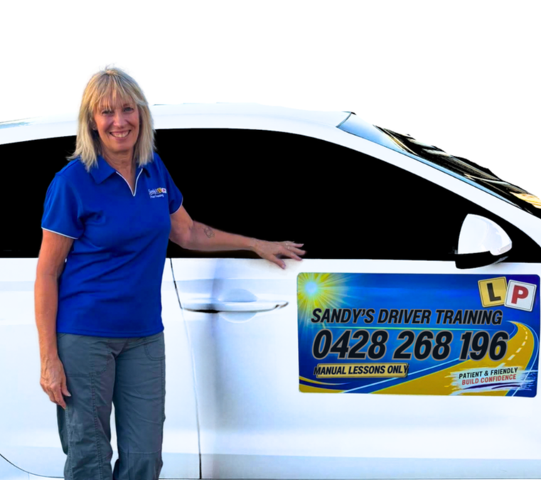 A woman standing next to a white car with a sign advertising Sandy's Driver Training on the door.