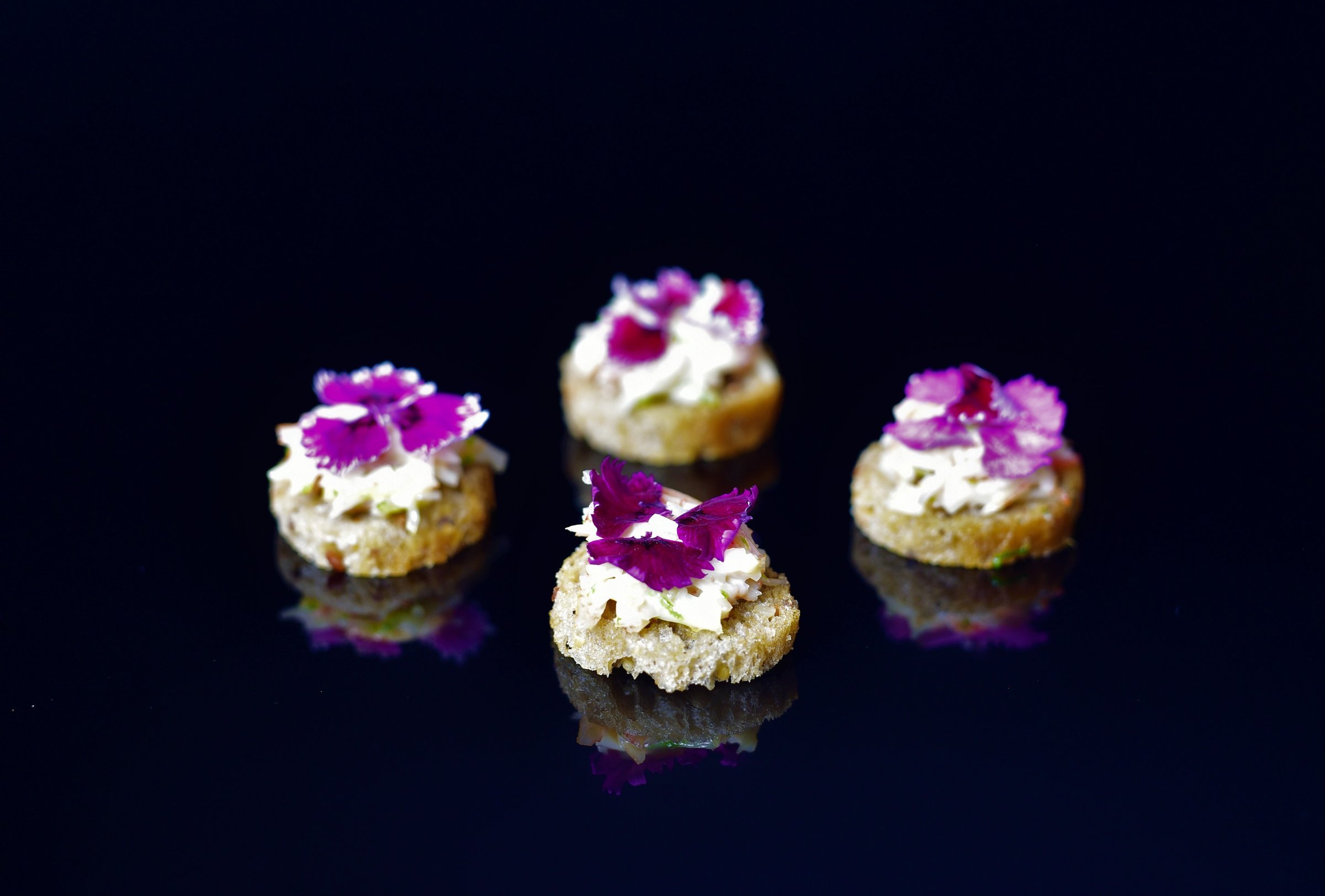 Canapés topped with purple flowers on a dark background
