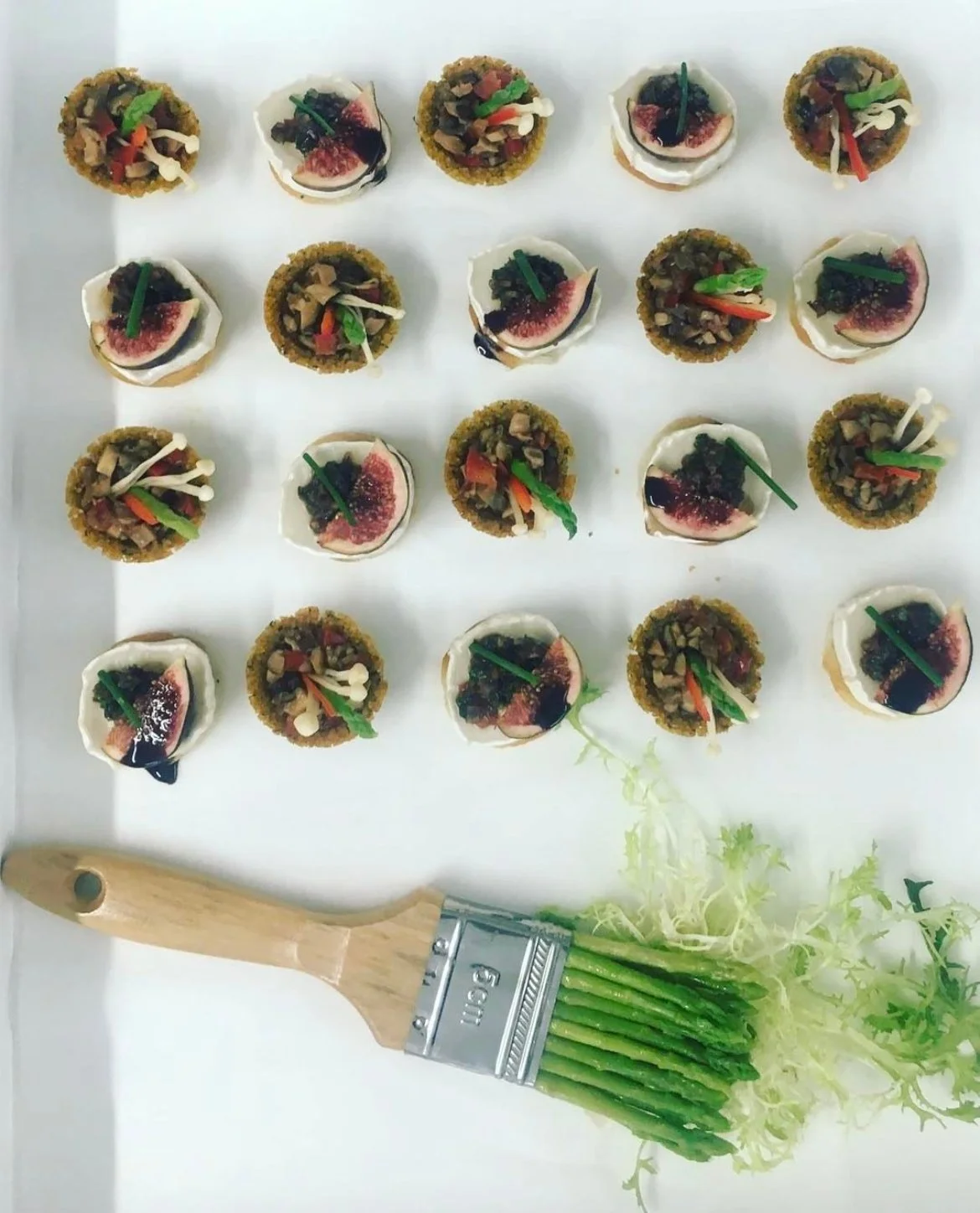 Tartlet canapés arranged in a grid with a herb brush