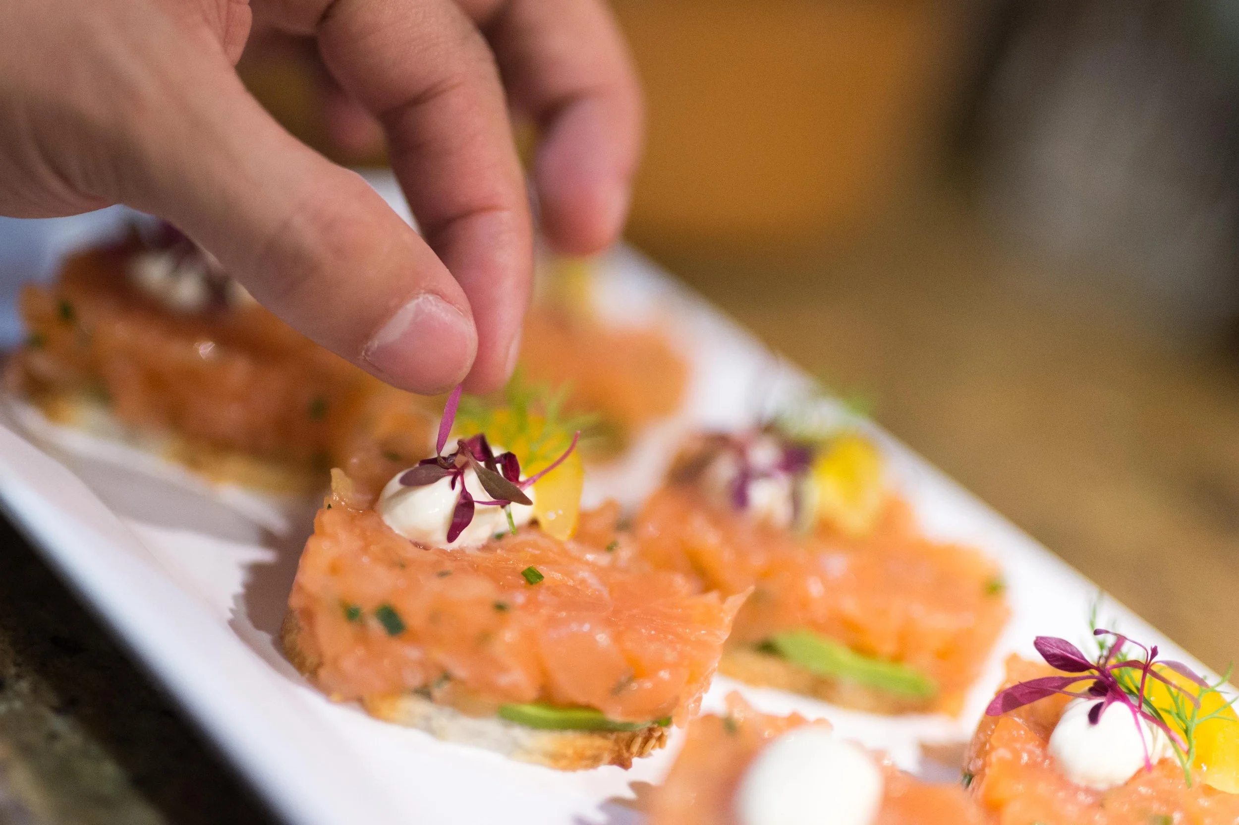 Hand garnishing salmon tartare canapés with edible flowers