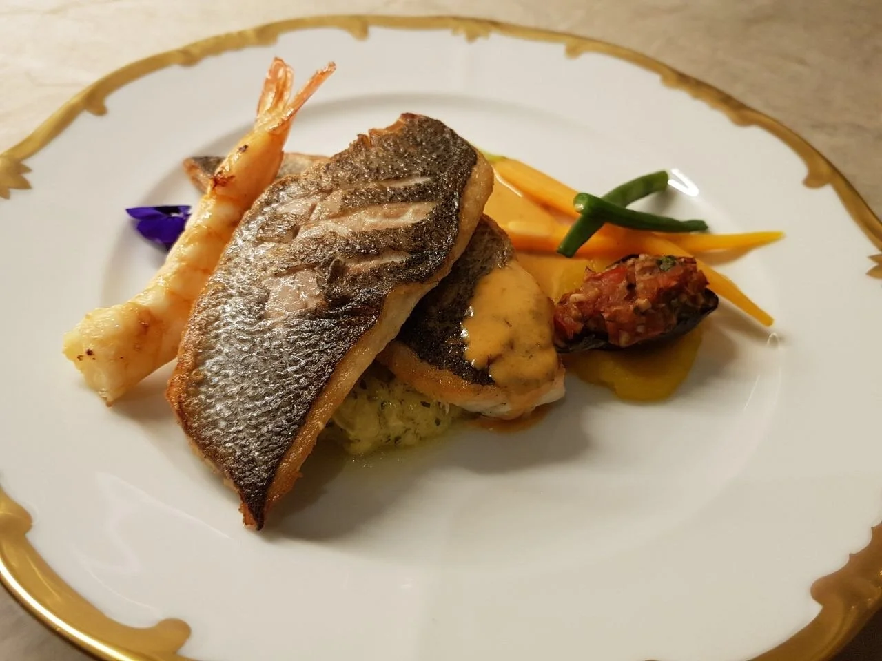 Pan-fried sea bass with prawn and vegetables on gold-rimmed plate