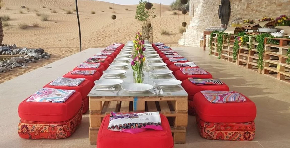 Long banquet table with red cushions set up in the desert