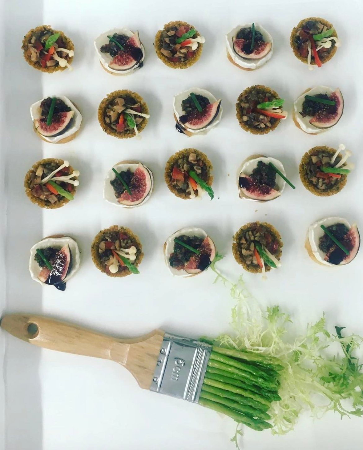 Tartlet canapés arranged in a grid with a herb brush