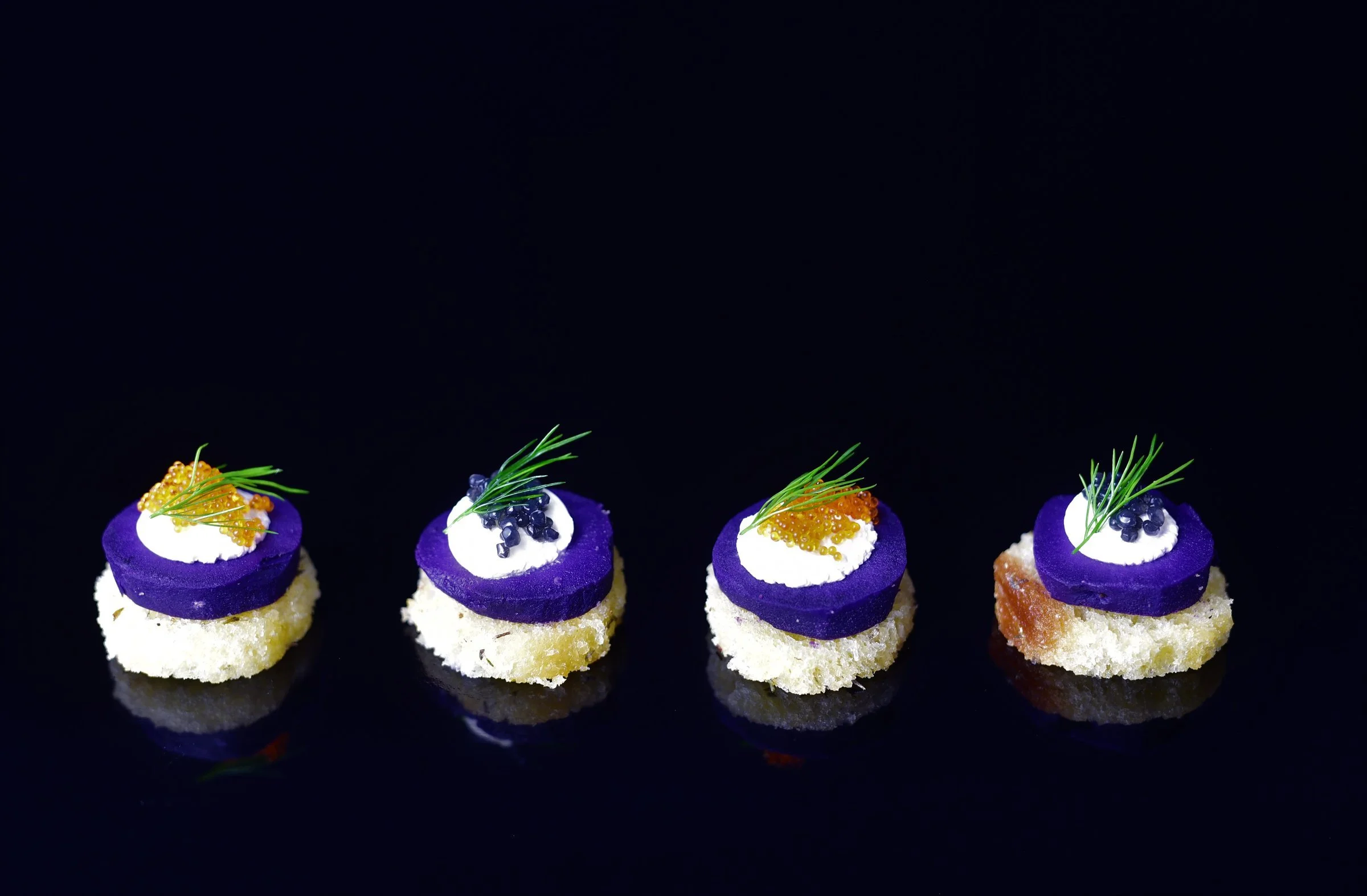 Four canapés topped with dill and roe on dark background