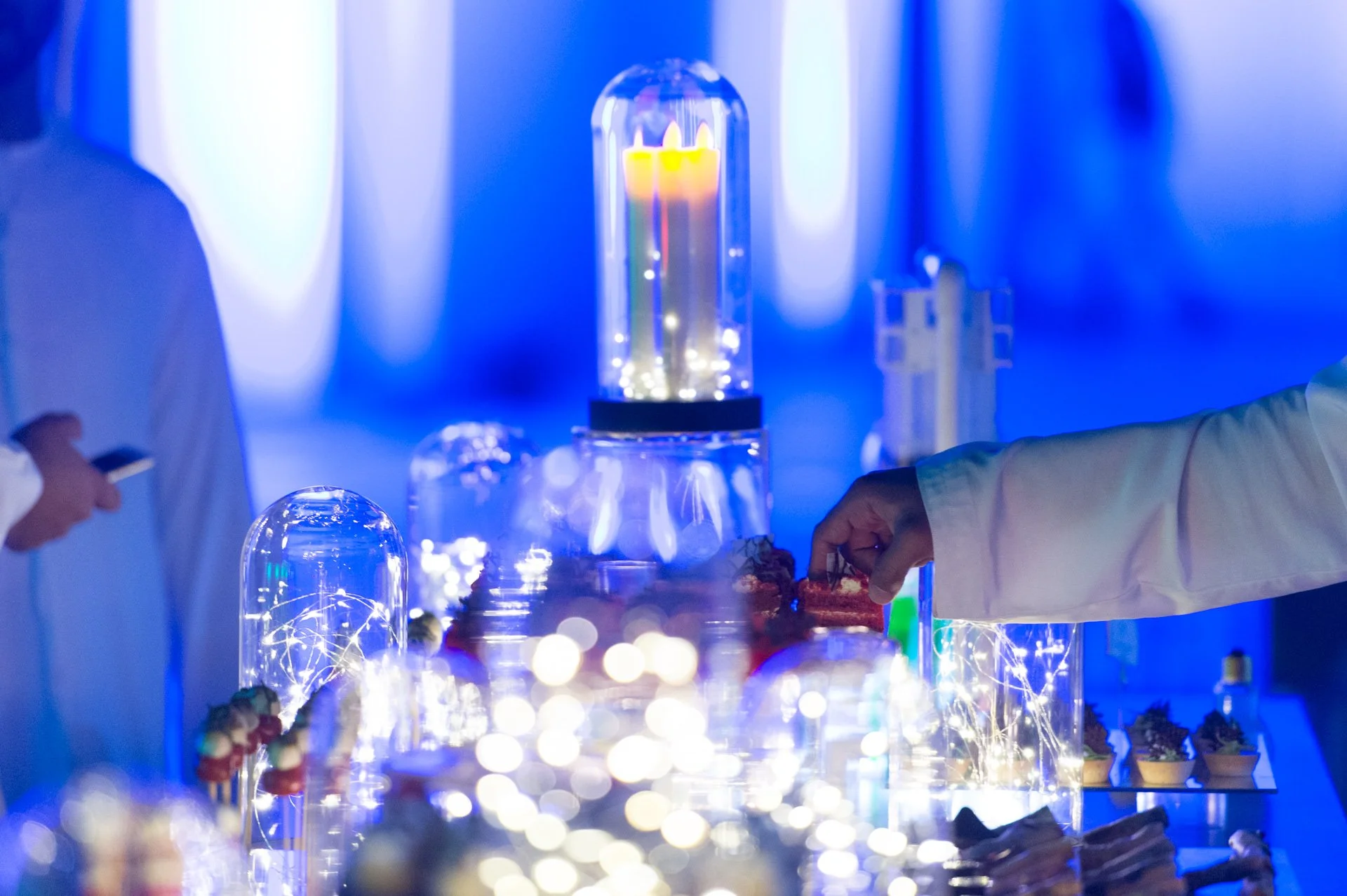 Guests at a blue-lit canapé table with glowing glass jars