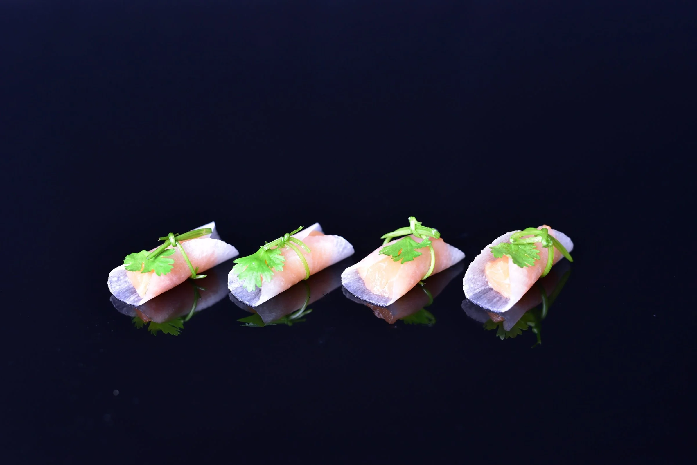 Four pastel canapés topped with micro herbs on black