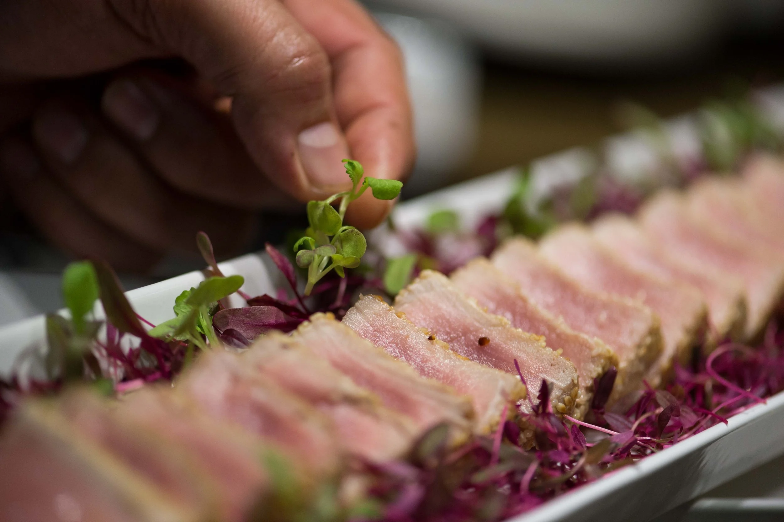 Sliced seared tuna canapés with micro herbs being garnished