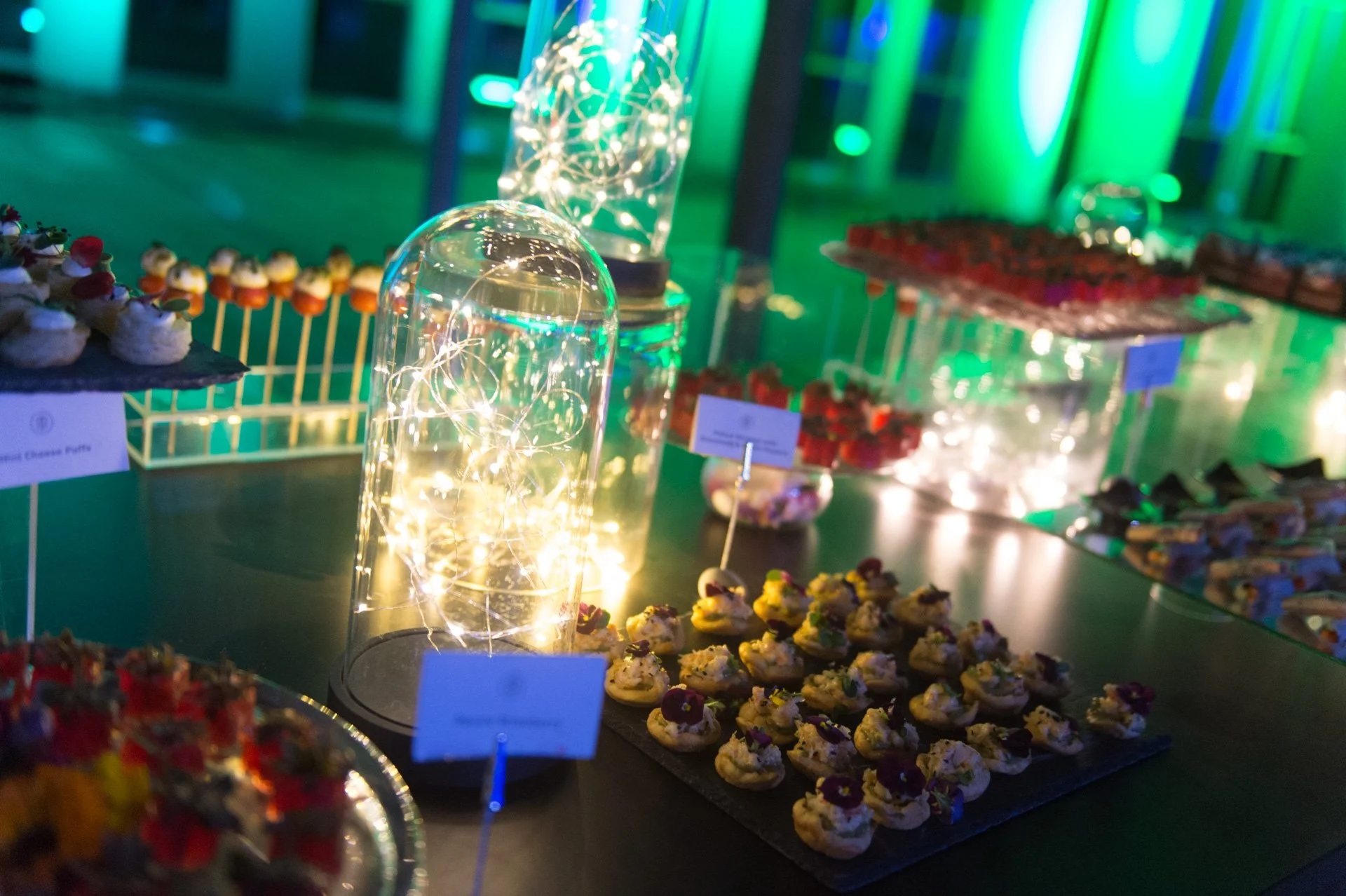 Canapé platters among glass cloches under green lighting