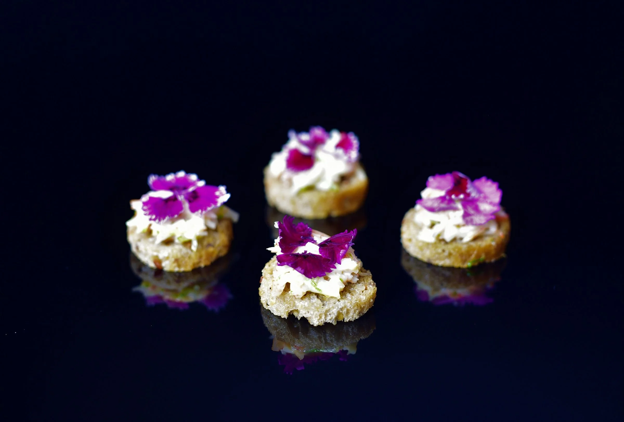 Canapés topped with purple flowers on a dark background