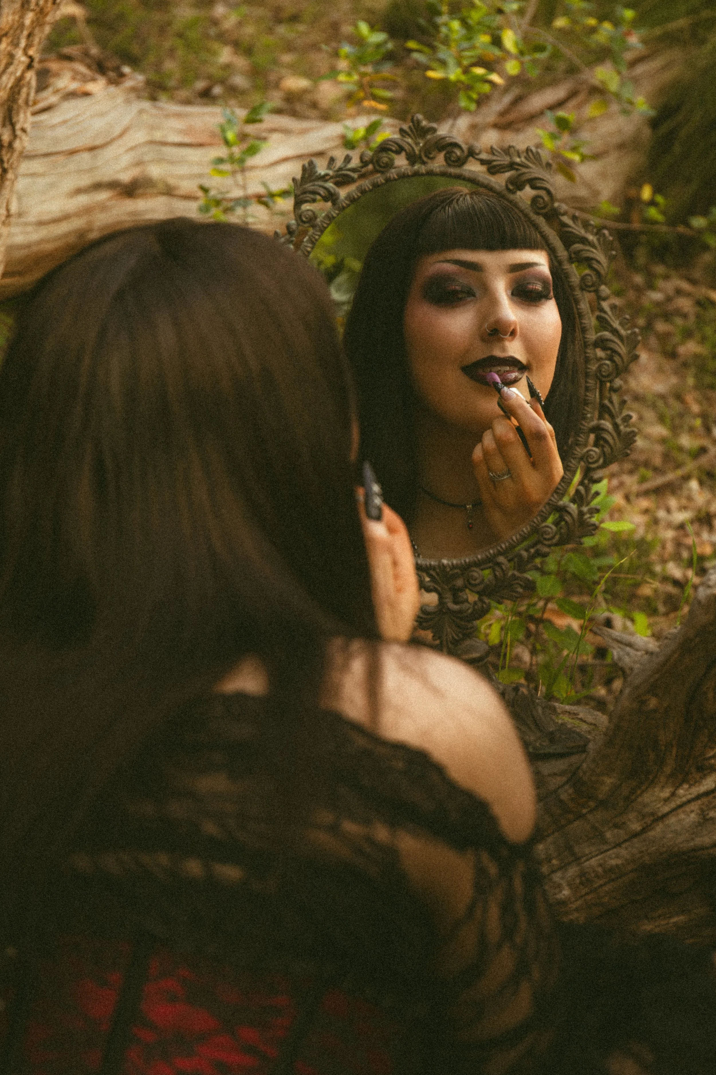 Alternative gothic woman applies lipstick in a mirror in the woods