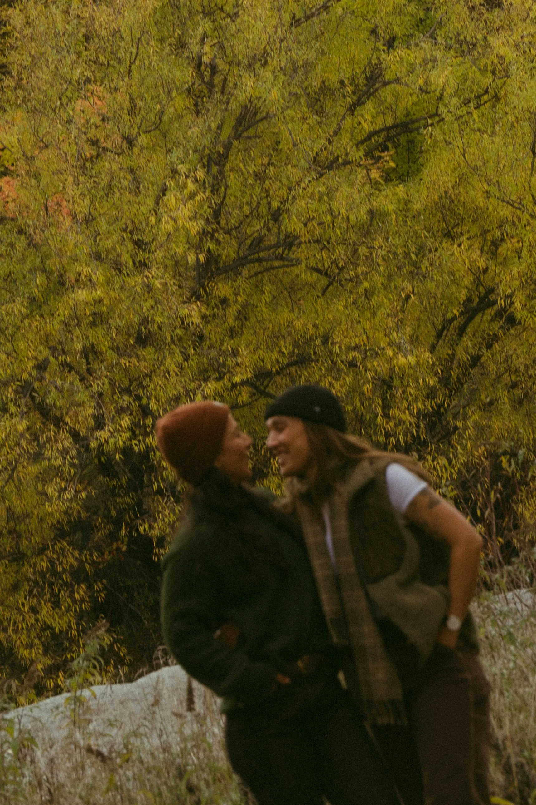 Two women smiling and laughing outdoors at night with trees illuminated in the background.