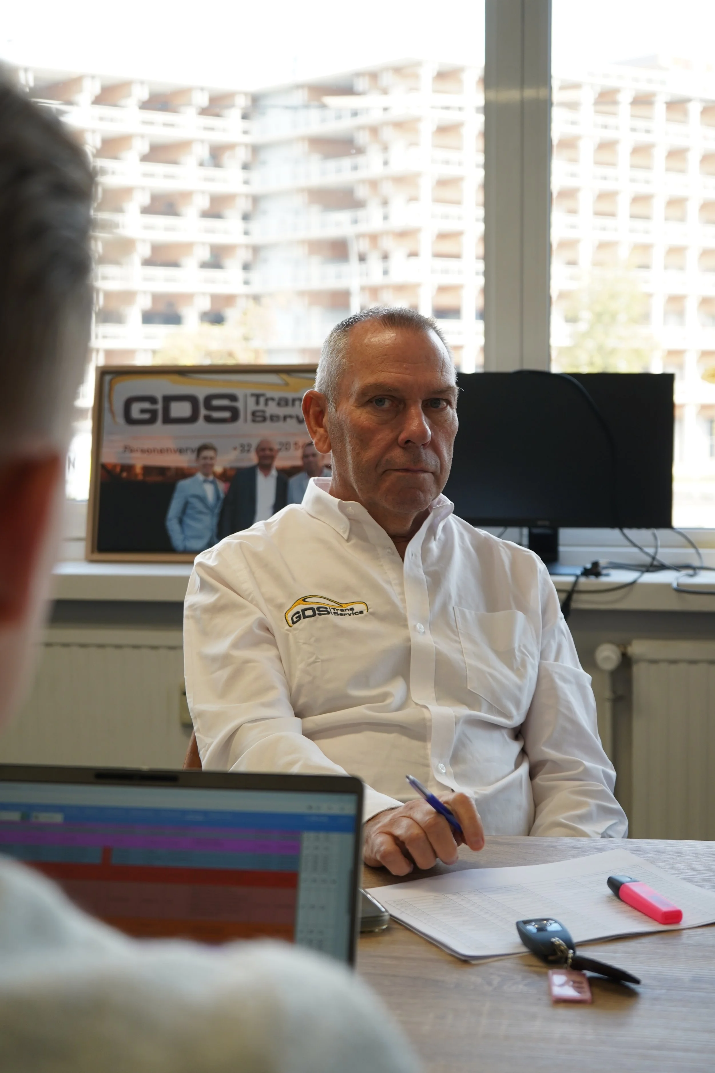 Guide van GDS Trans Service-overhemd werkt aan een bureau met laptop en technische tekeningen.