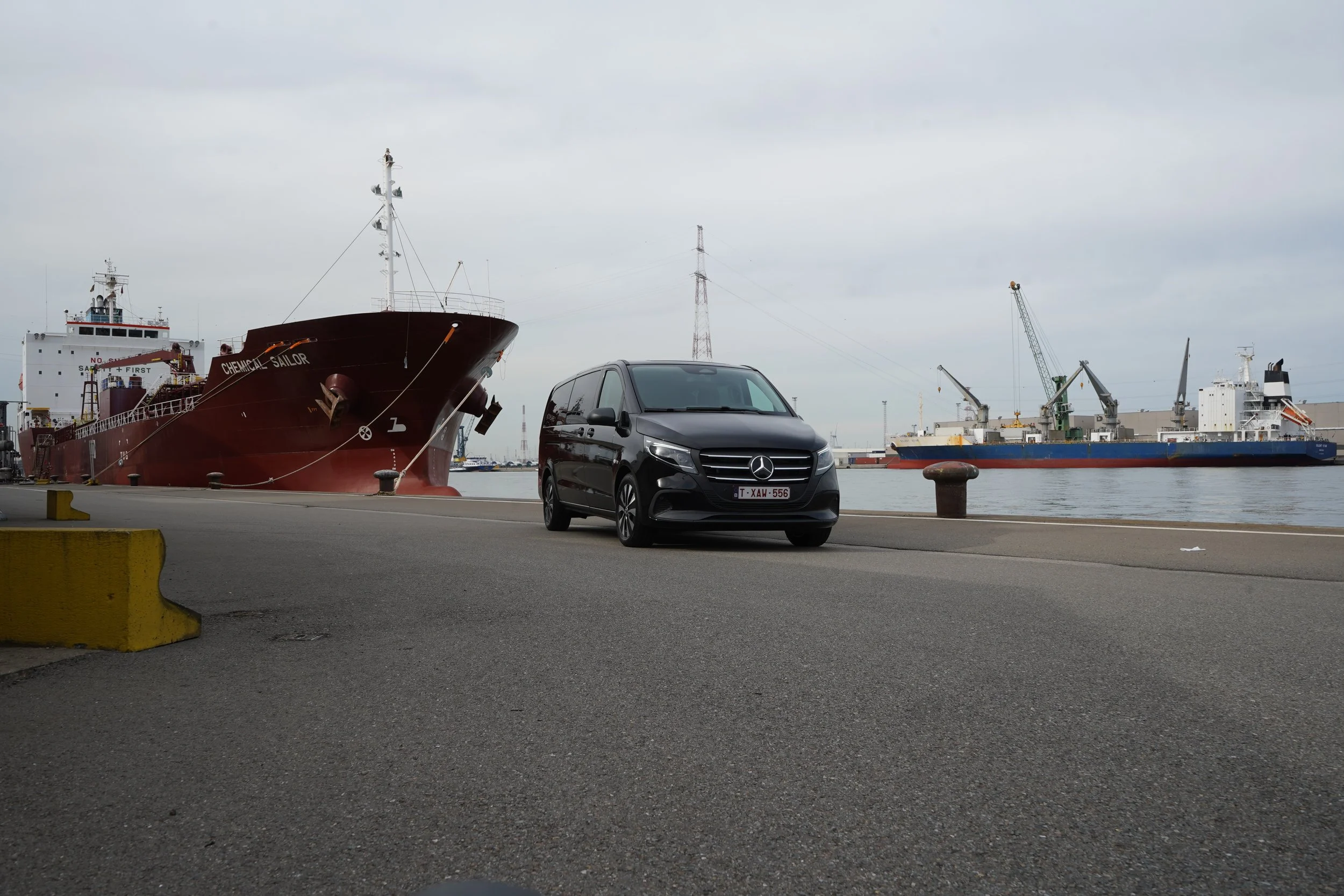 GDS Trans Service met zwarte Mercedes-Benz bestelwagen op een kade in een industriële haven, met vrachtschepen en havenkranen op de achtergrond.