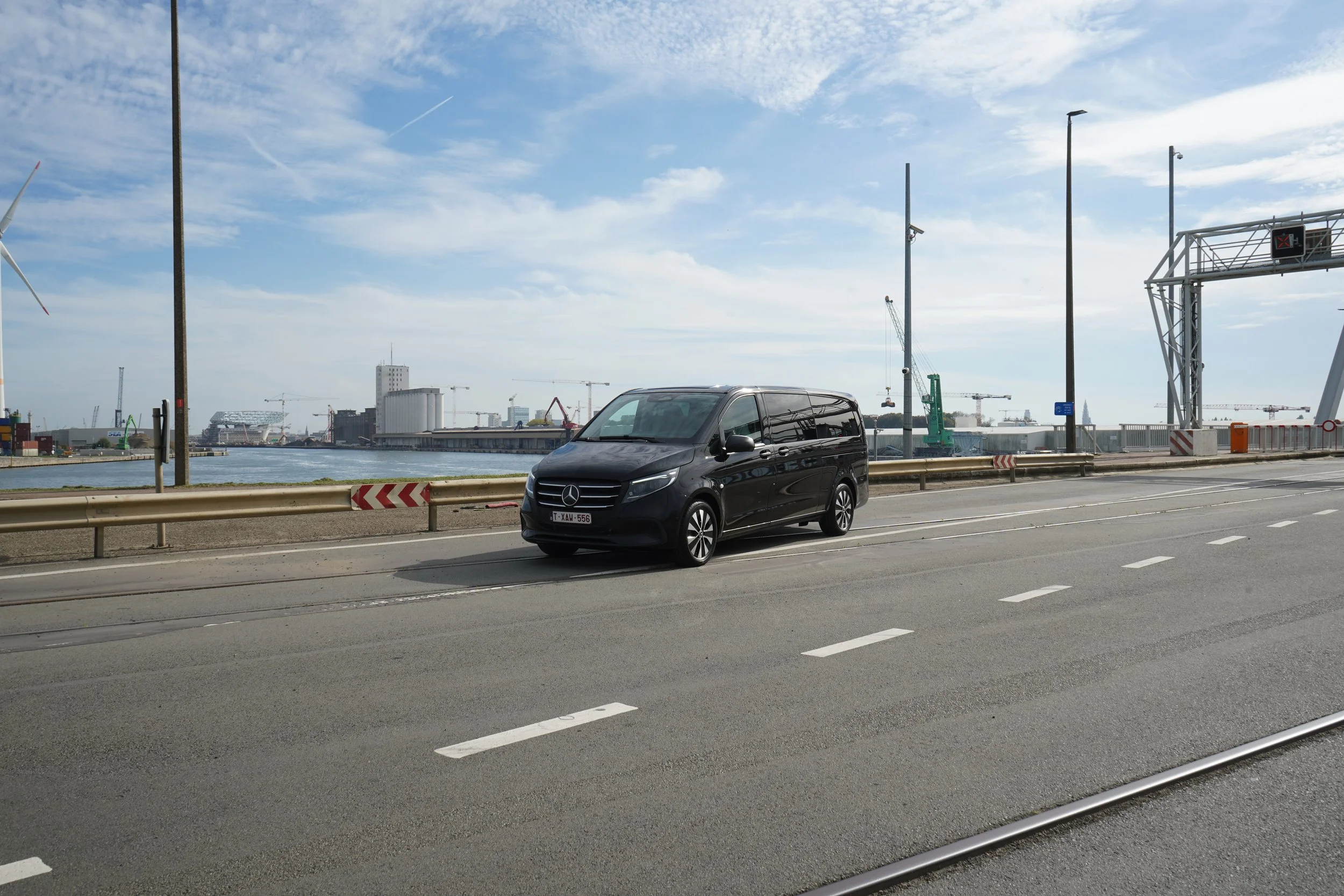 Zwarte Mercedes-Benz V-Klasse op een stadsweg langs een haven met kranen en water.