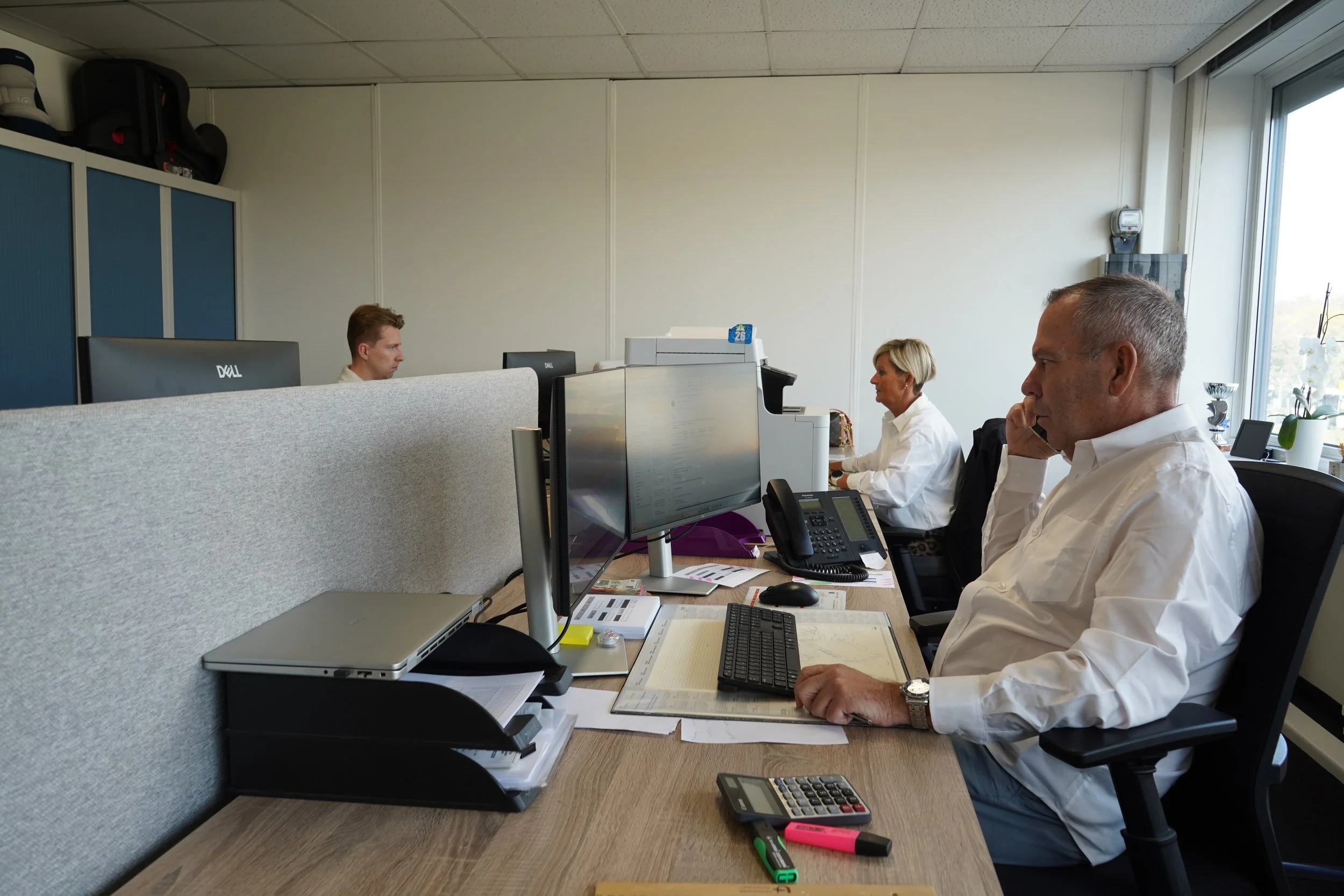 Kantoor met drie medewerkers van GDS Trans Service achter computerschermen en bureaus met documenten, telefoons en kantoorbenodigdheden.