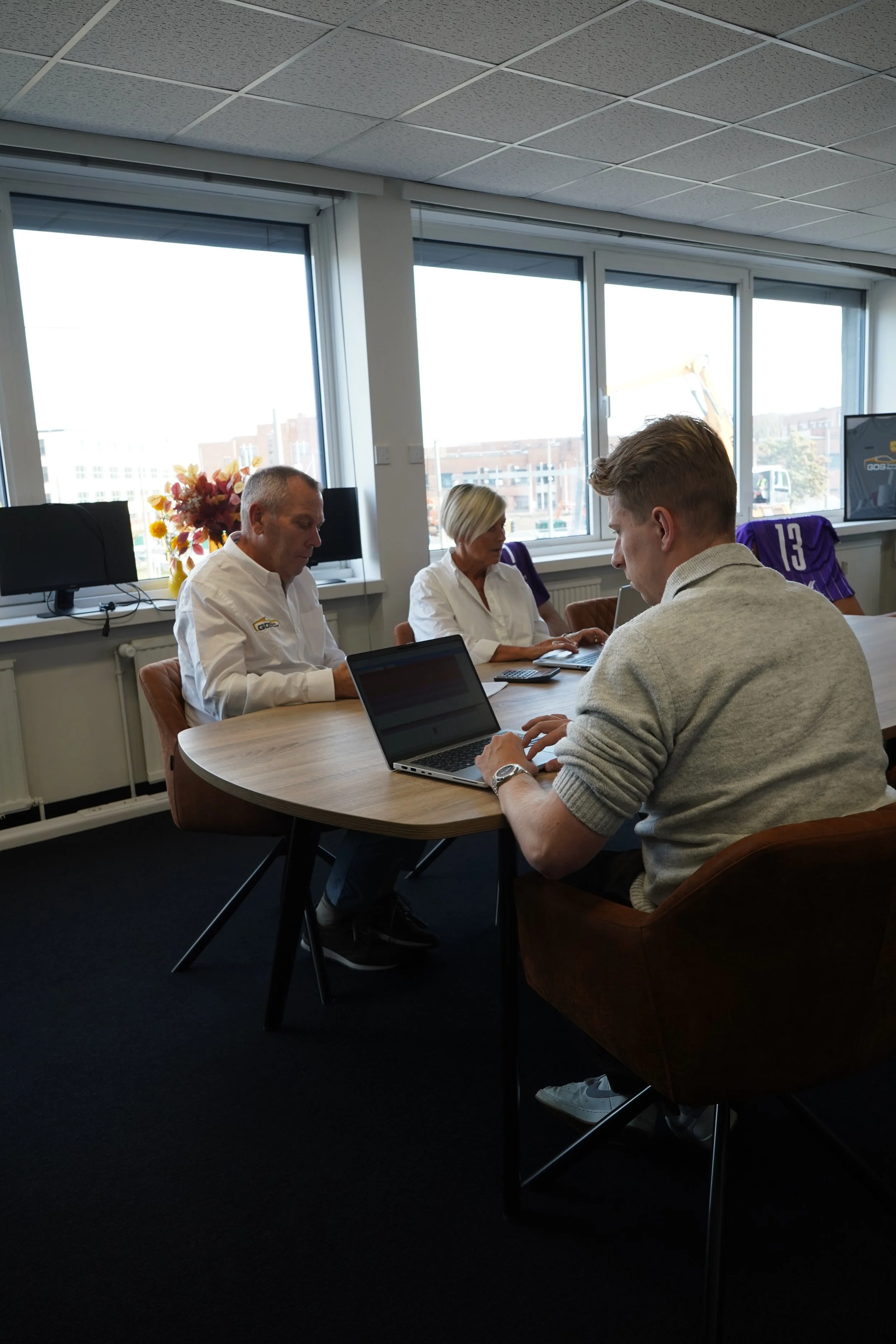 Team van GDS Trans Service vergaderen aan een tafel in een kantoor, met laptops en grote ramen op de achtergrond.
