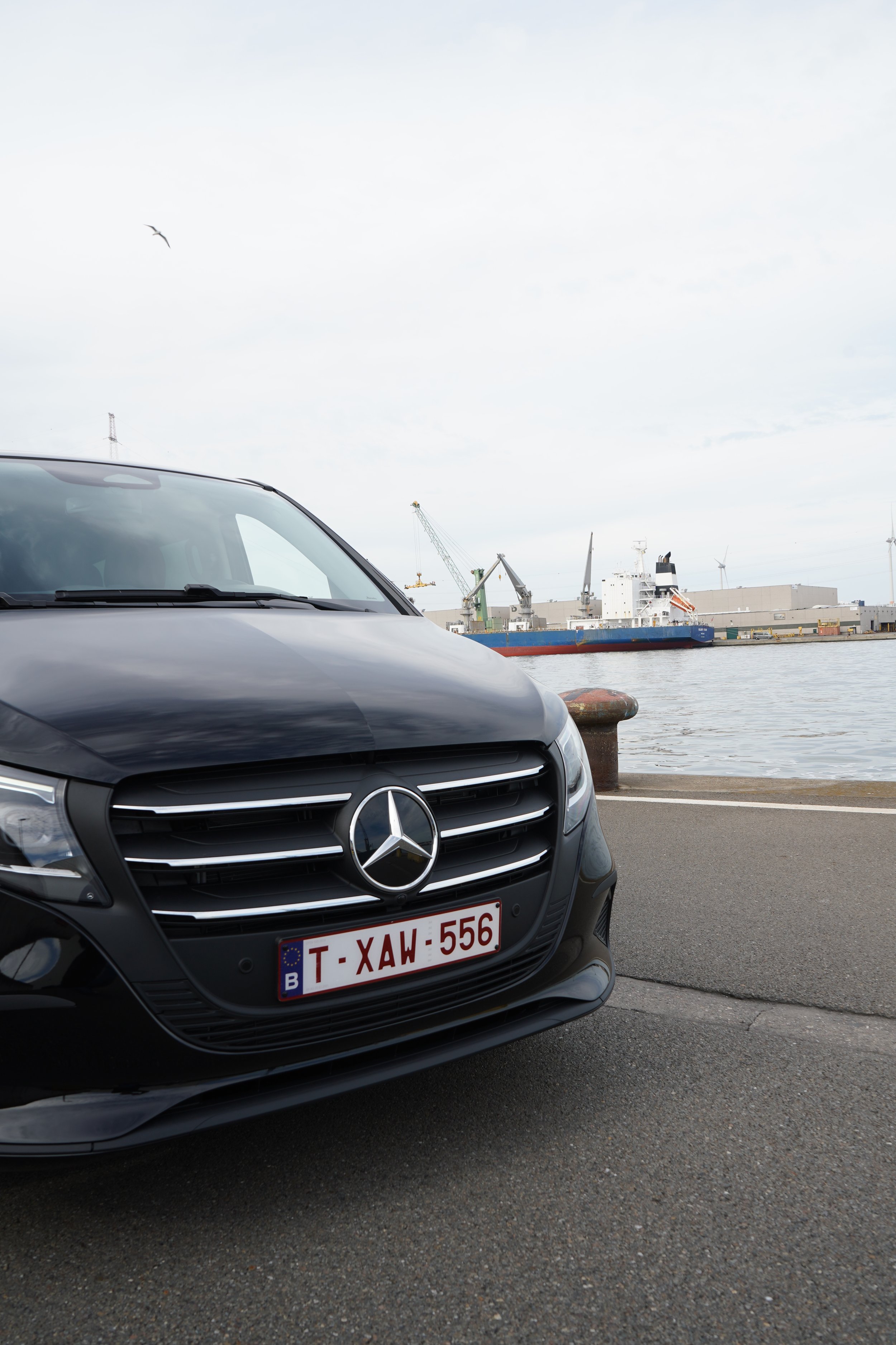 Zwarte Mercedes van GDS Trans Service voor een vrachtschip in een industriële haven met kranen en windturbines.