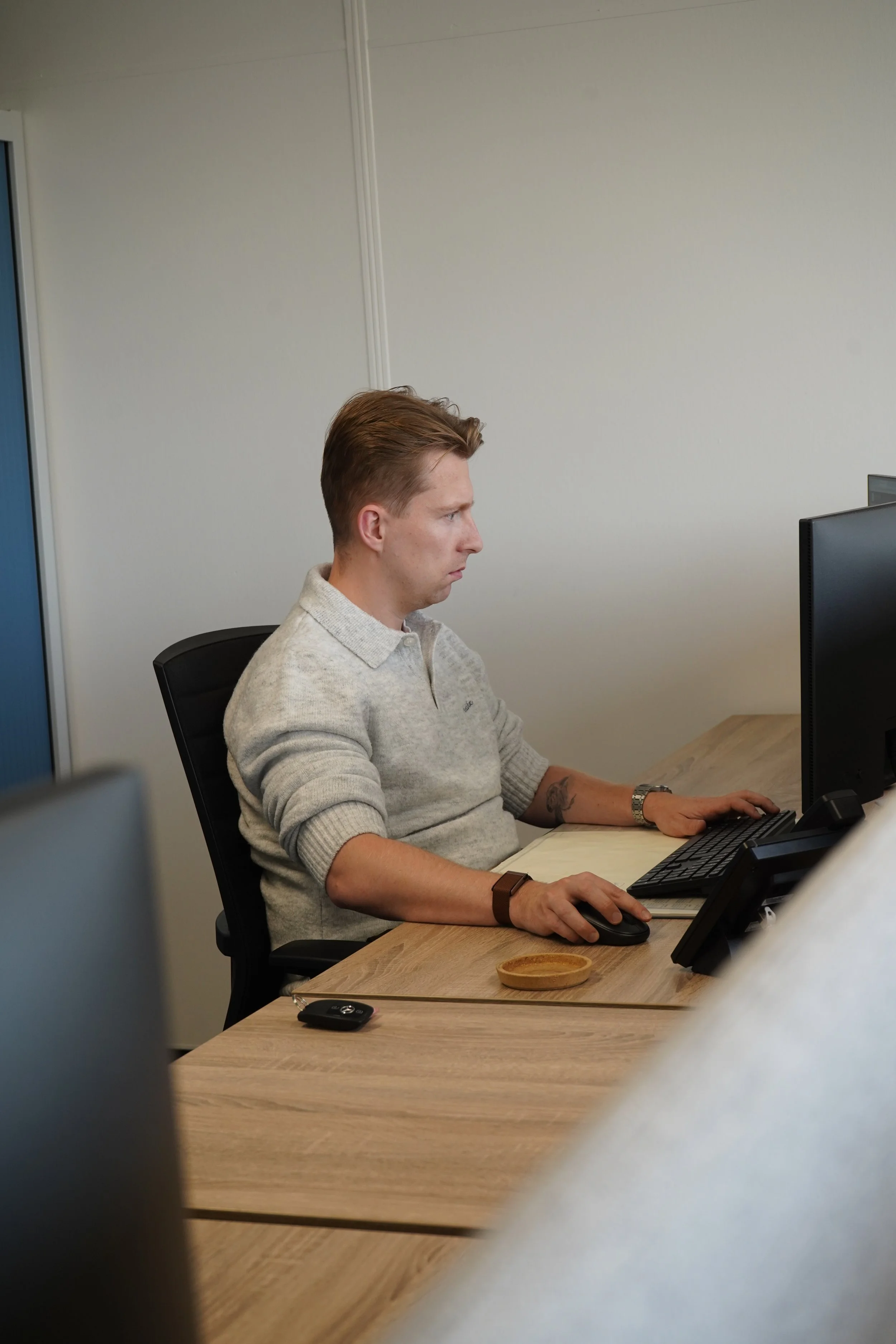 Andy van GDS Trans Service zit achter een computer aan een houten bureau en gebruikt een muis en toetsenbord.