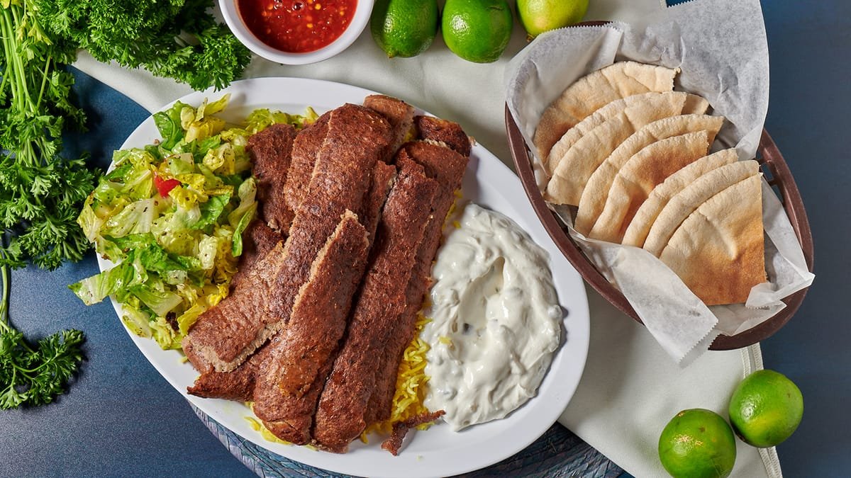 Fried fish fillets with yellow rice, lettuce salad, tartar sauce, and pita bread with lime wedges and salsa in the background.