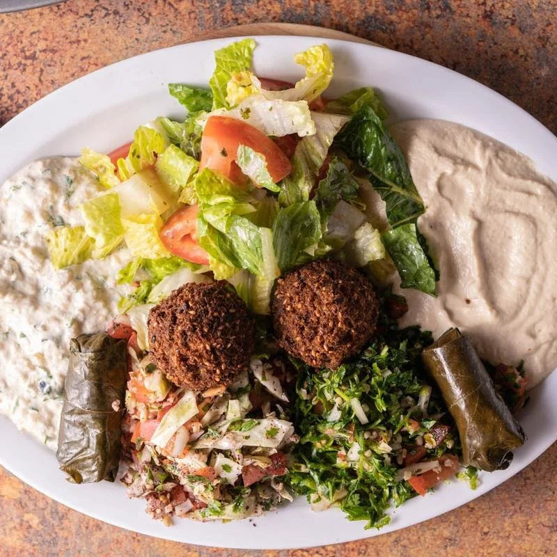 Plate of Mediterranean food with falafel, tabbouleh, grape leaves, hummus, and salad.