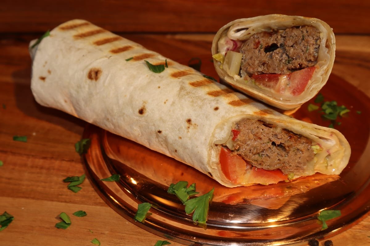 A burrito cut in half on a glass plate, showing meat, vegetables, and lettuce inside.