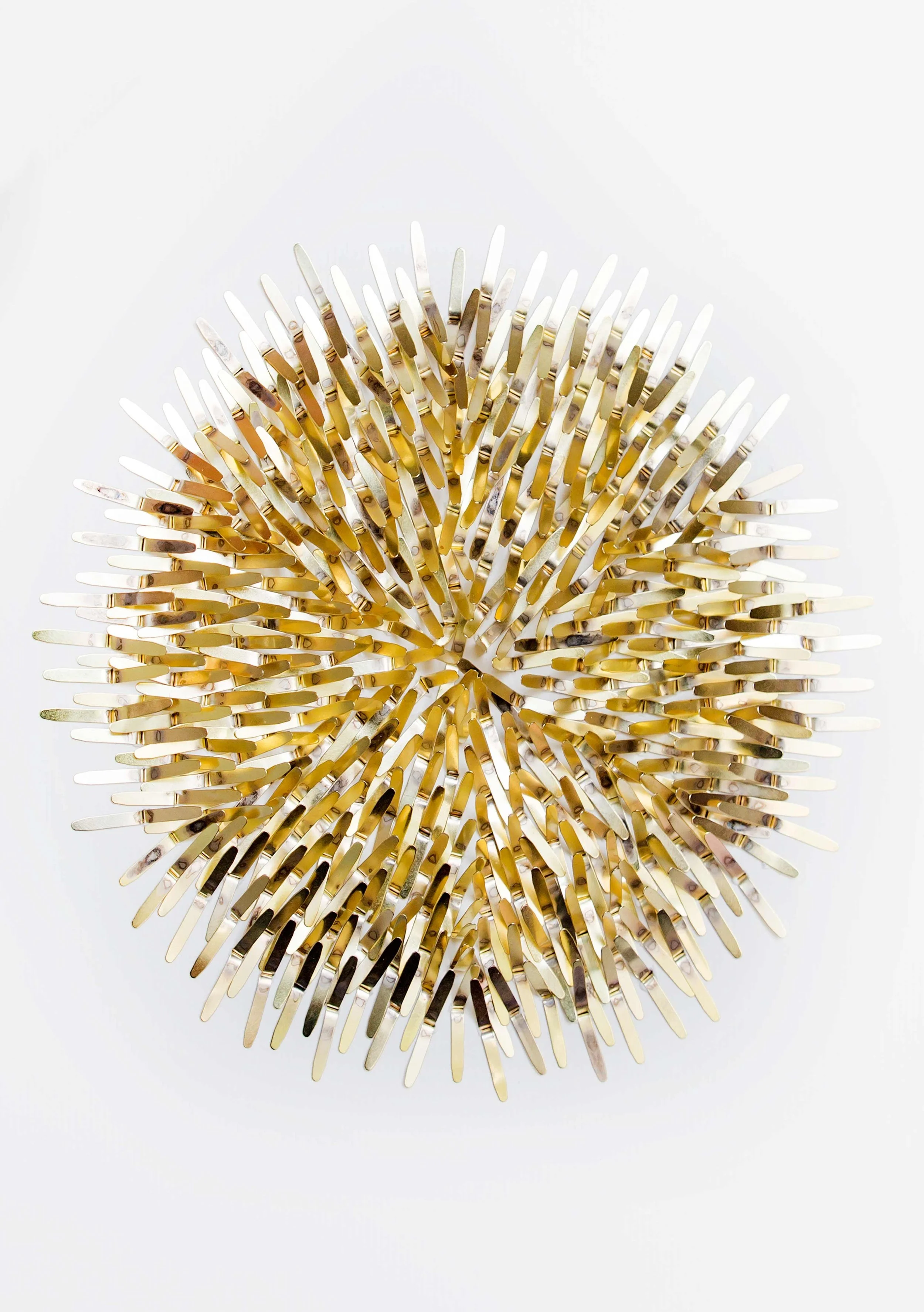 Un objet décoratif en forme de sphère composée de nombreuses épingles dorées et blanches, placé sur un fond blanc.