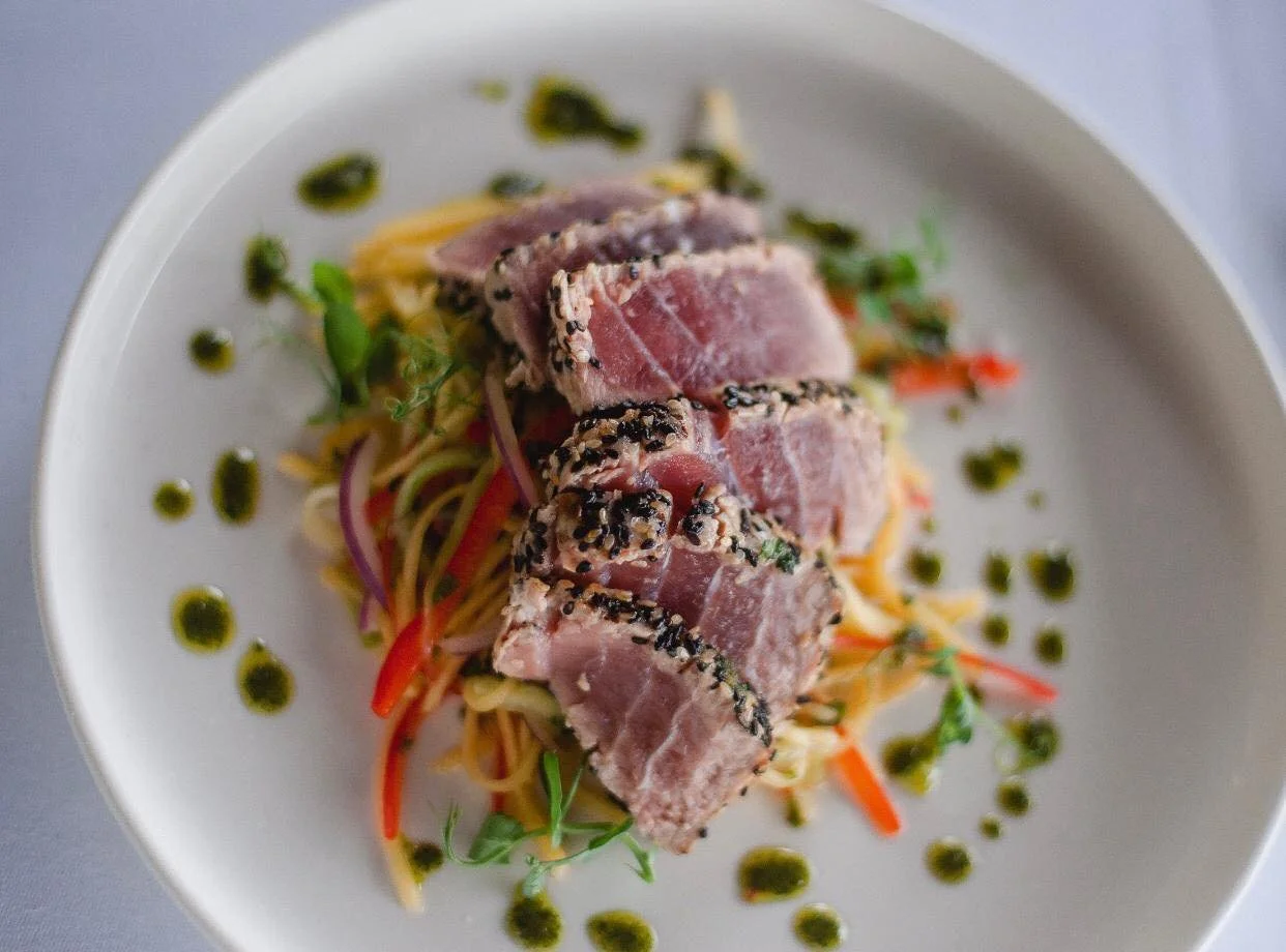 Ein Teller mit rohem Thunfisch auf einem Gemüsesalat, dekoriert mit grüner Soße.