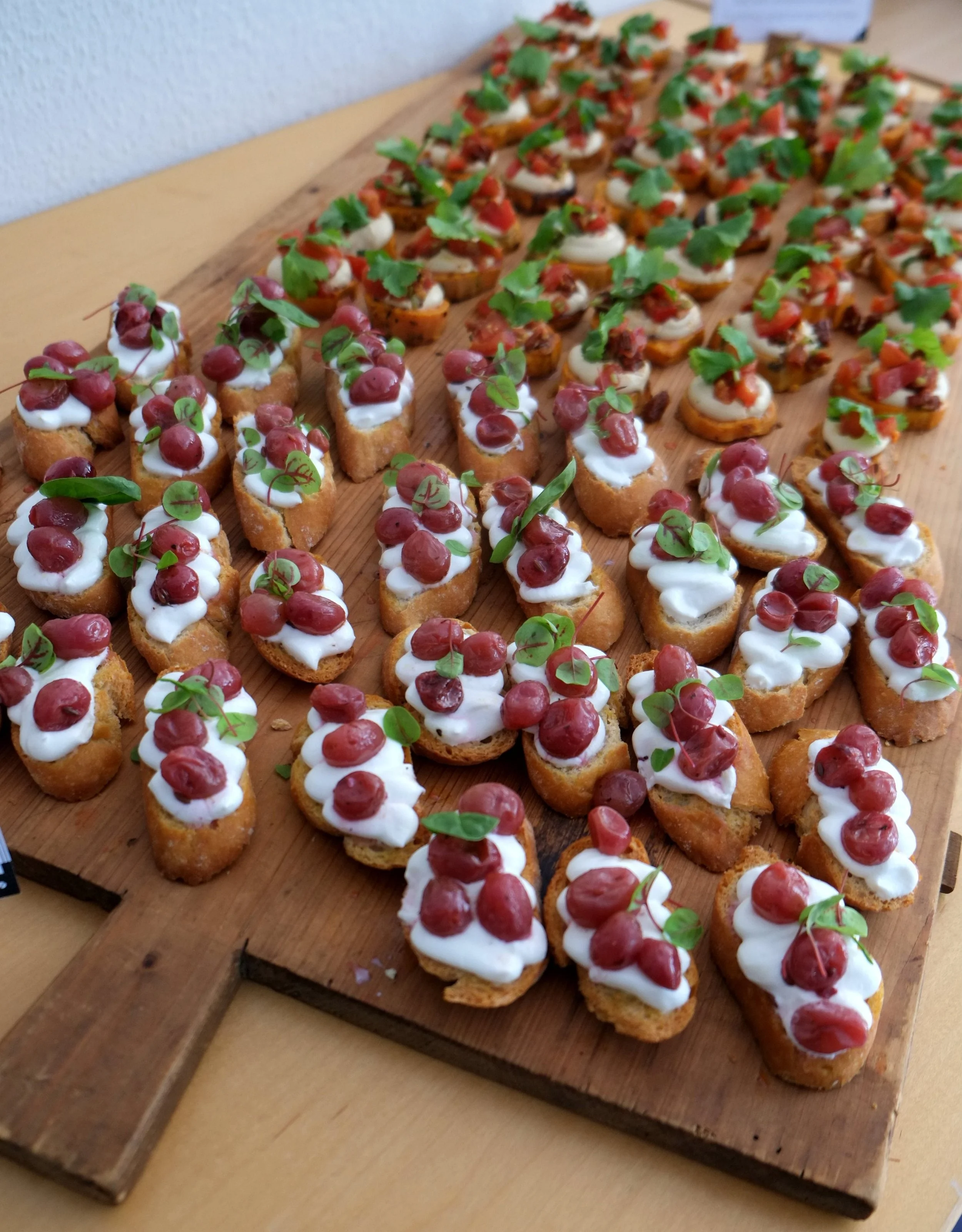 Verschiedene Canapés mit Crème, Kirschen und frischen Kräutern auf einem Holzbrett.