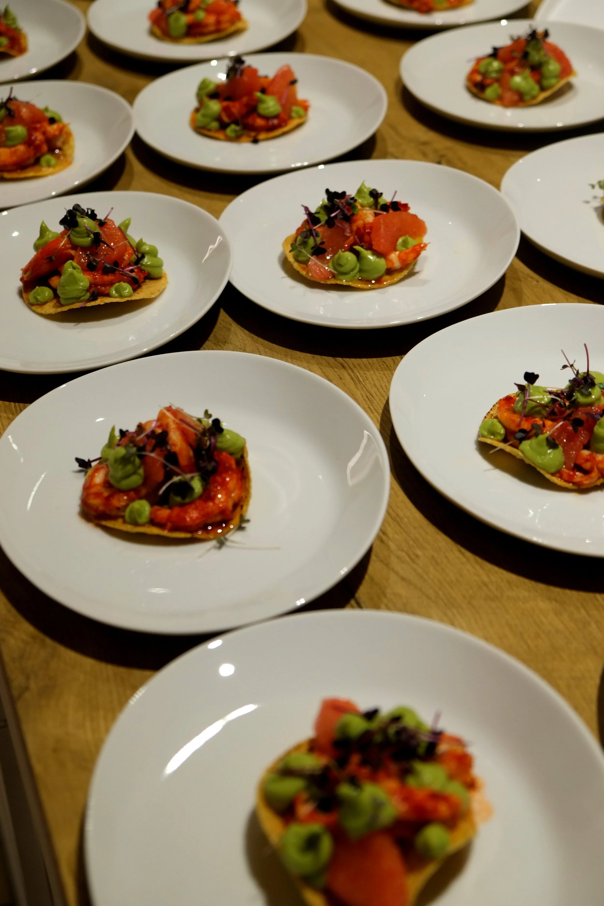 mehrere kleine Torten mit Lachs, grünem Kräuterpüree und schwarzen Sämereien auf weißen Tellern
