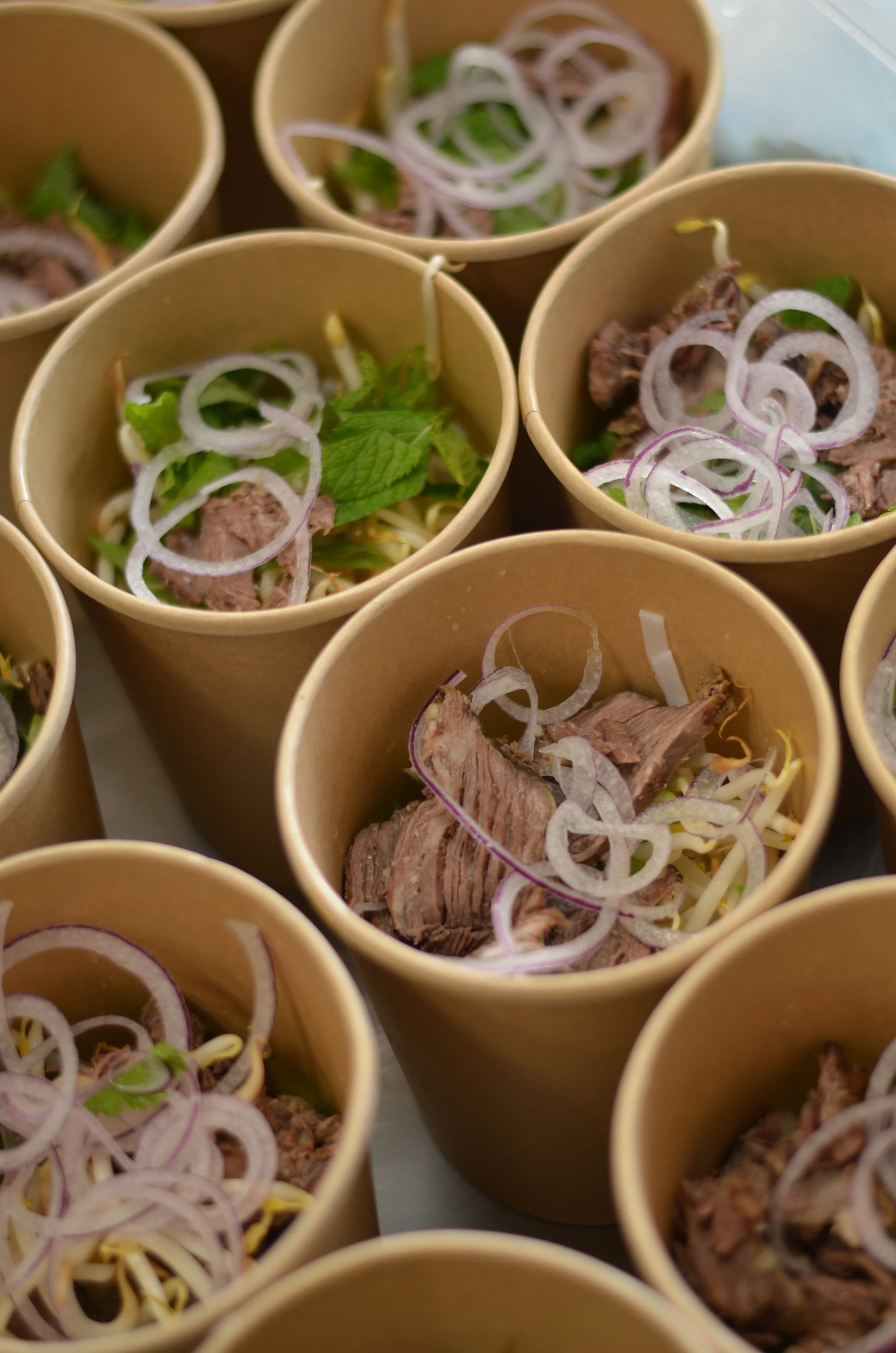 Mehrere Pappbecher mit Rindfleisch, Zwiebelringen und grünem Salat