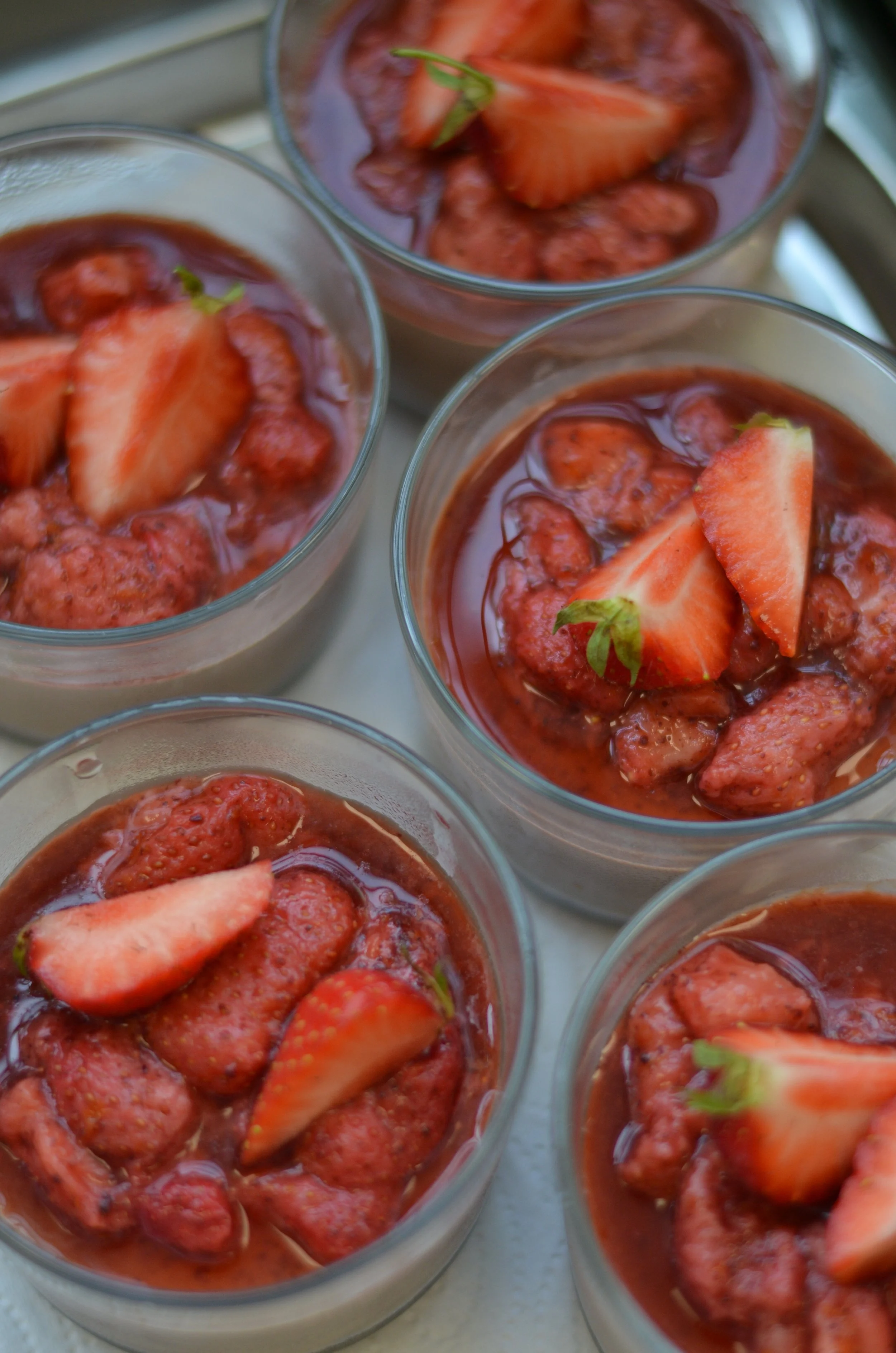 Vier Gläser mit Erdbeeren und Erdbeerscheiben, gefüllt mit Erdbeerpüree oder -joghurt.