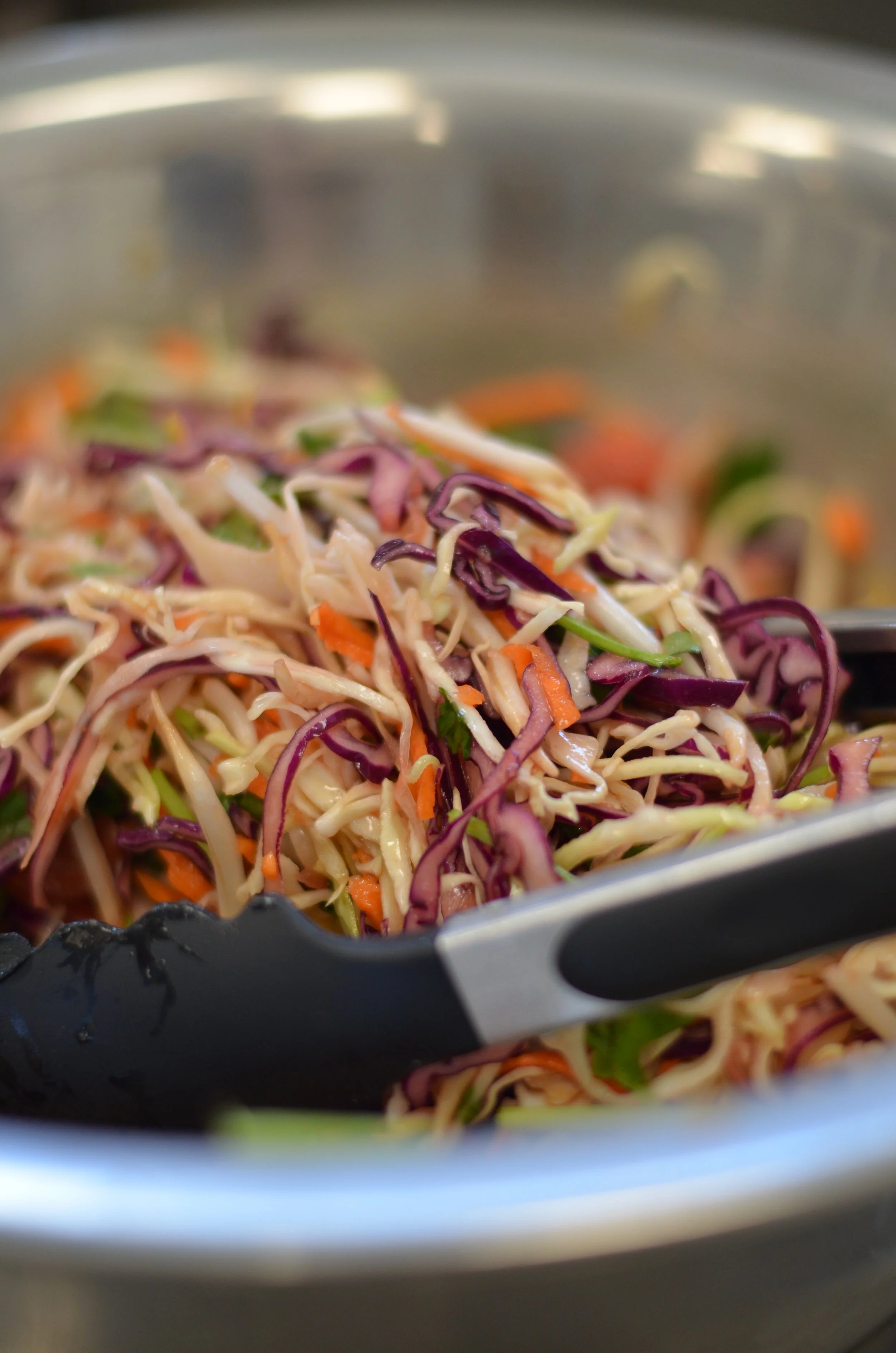 Bunte, geschnittene Gemüsesalat in einer Schüssel, Tongs zum Servieren im Vordergrund.