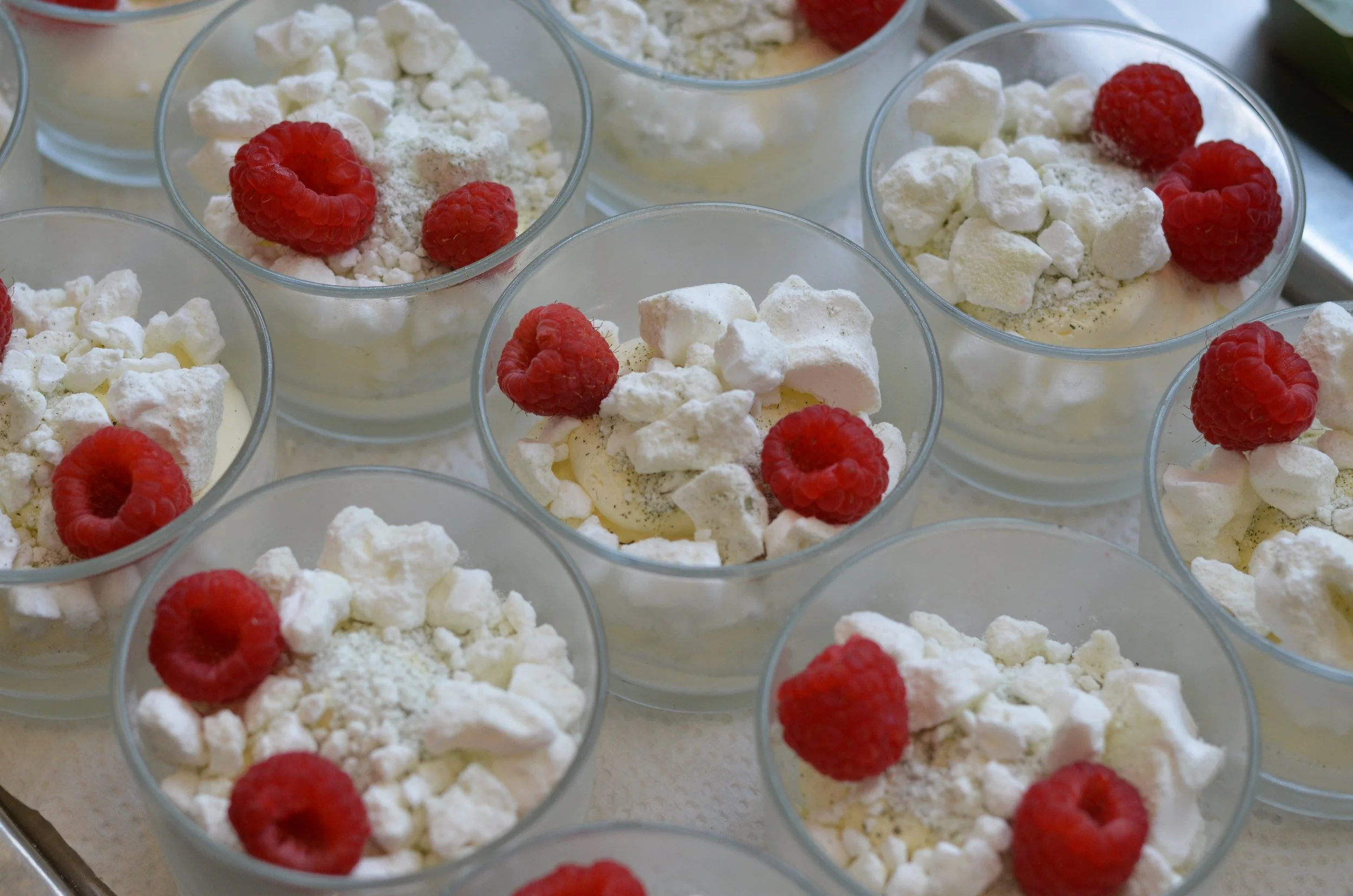 Mehrere Gläser mit Schlagsahne, garniert mit Himbeeren, Meringo-Schnitten und Puderzucker.