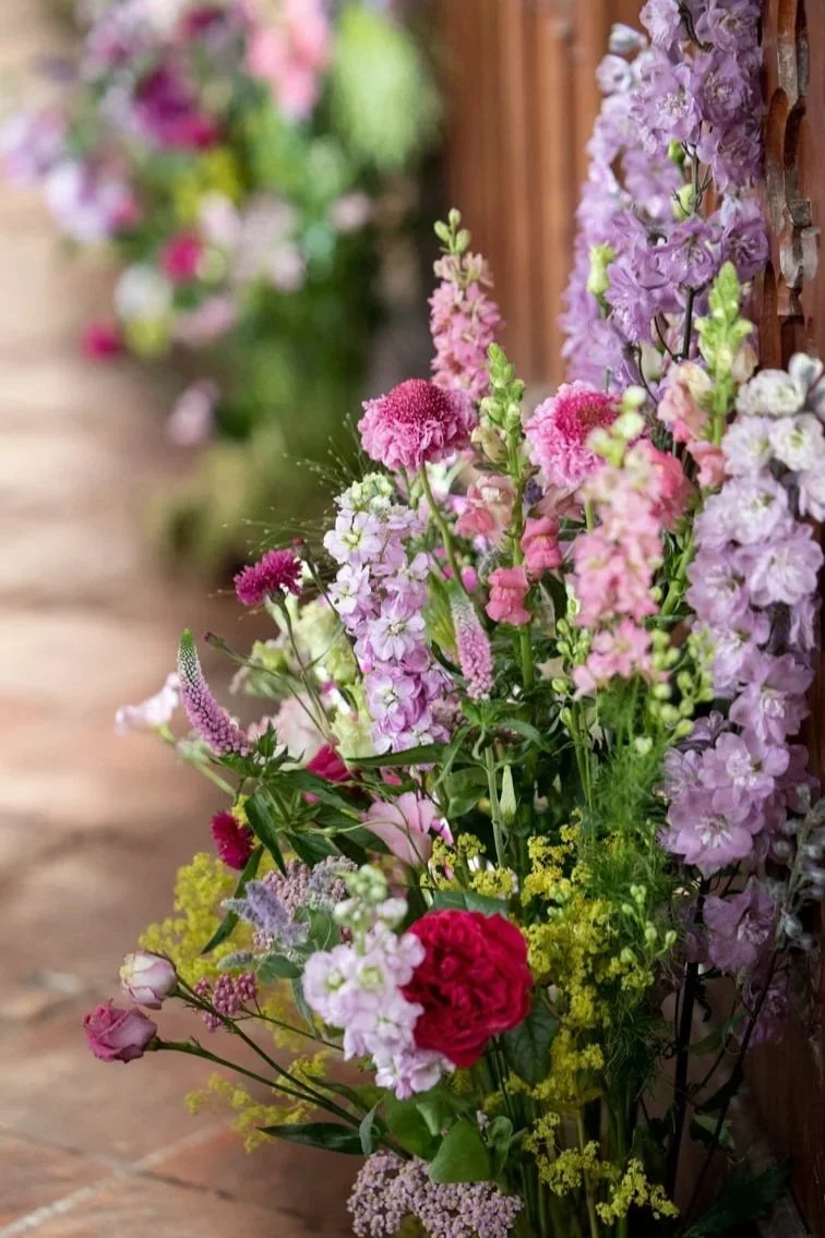 Colorful bouquet of pink, purple, and red flowers leaning against a wooden wall.